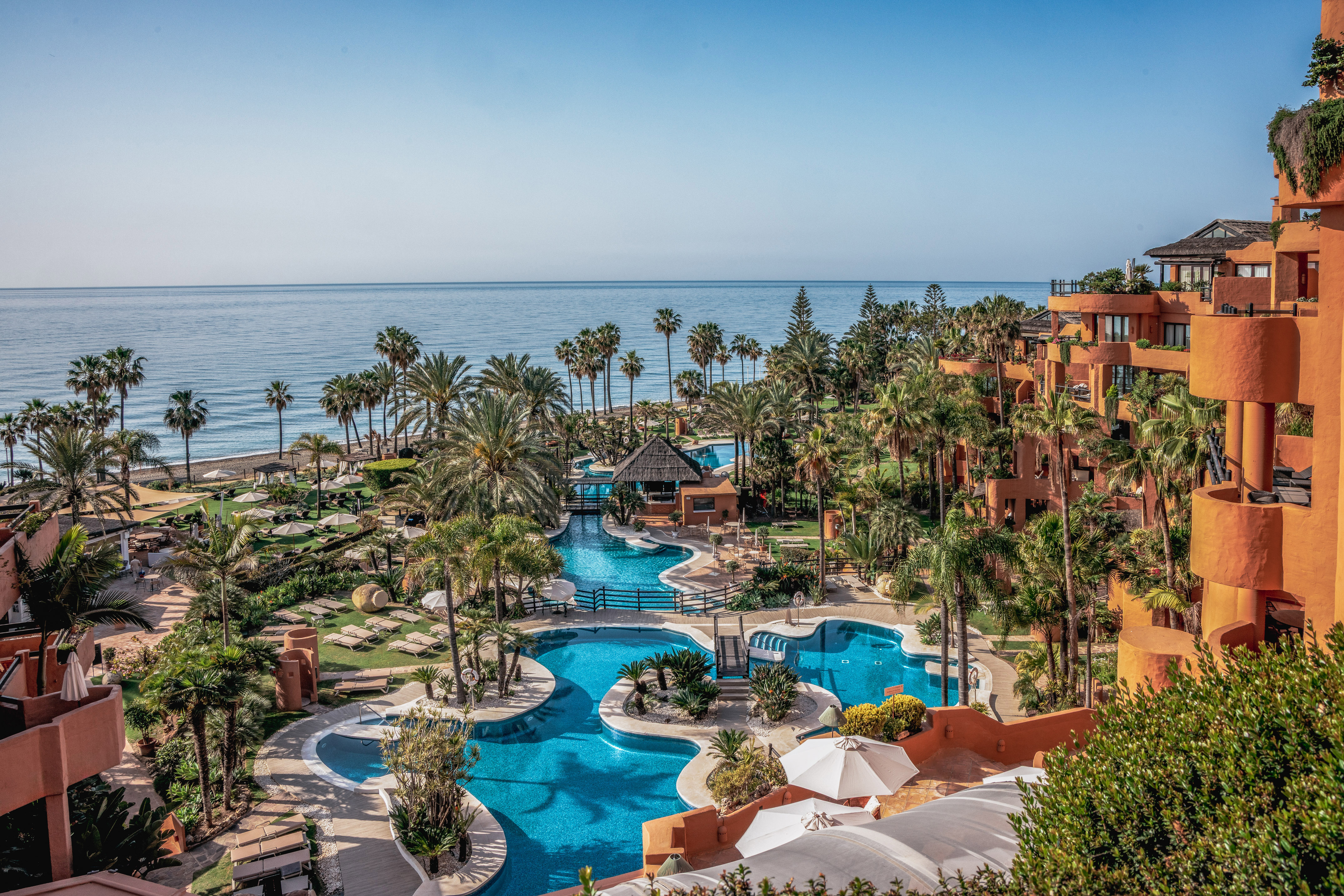 Oceanfront resort with winding blue pools, palm trees, and terracotta hotel buildings.