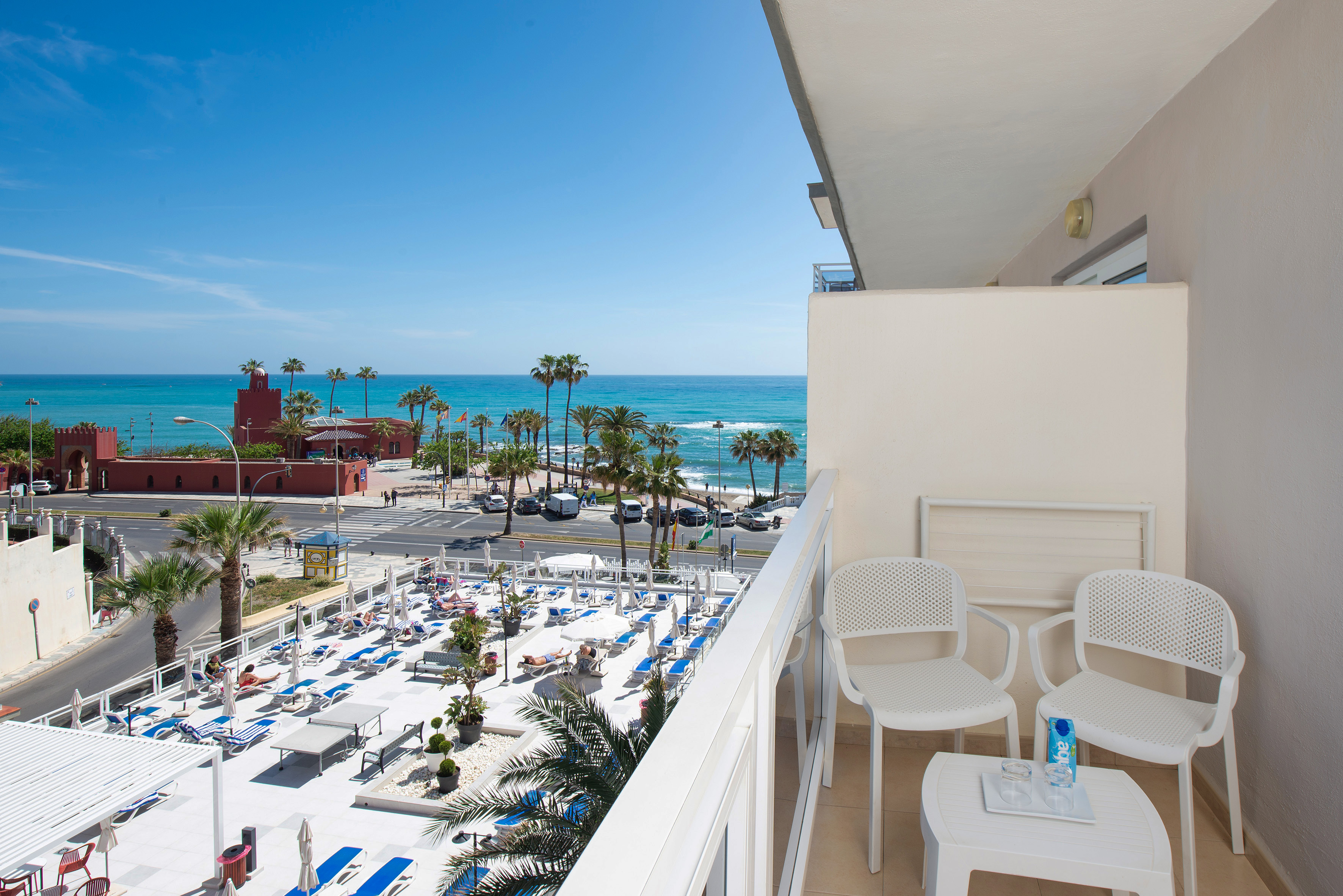 Hotel balcony overlooking turquoise sea, palm trees, and beachfront sun deck.