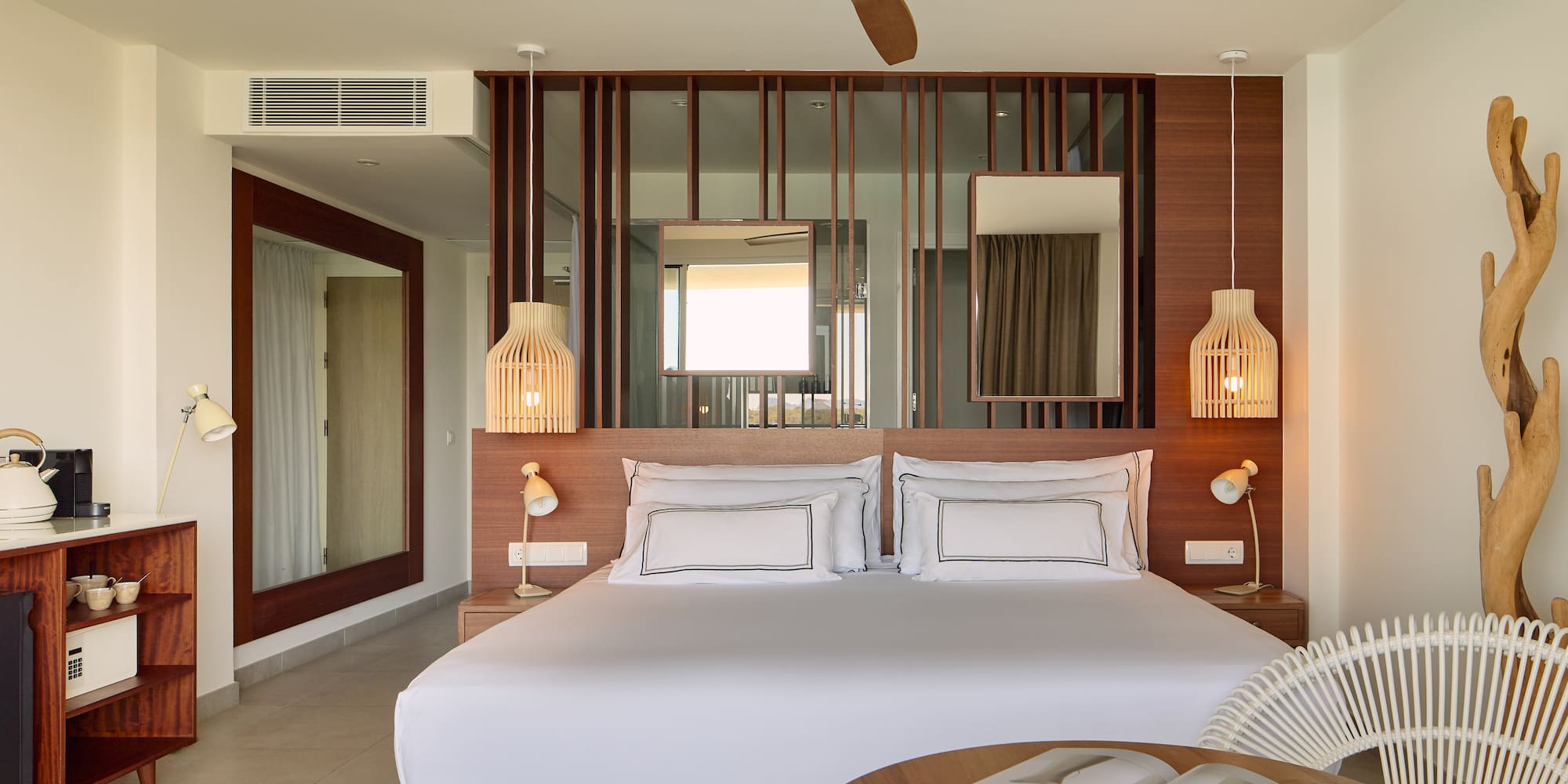 Modern hotel bedroom with king bed, wooden decor, ceiling fan, and rattan chair.
