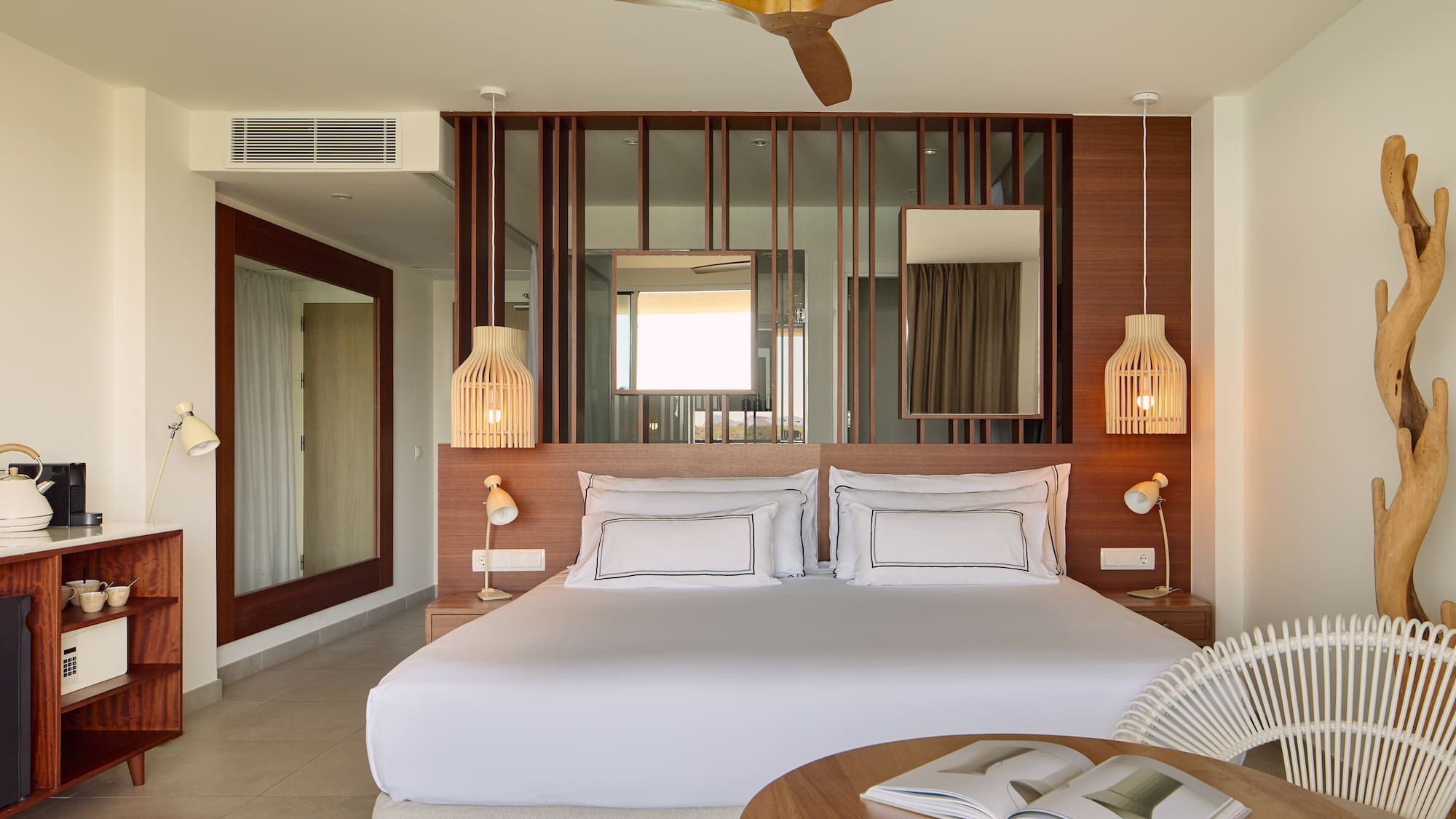 Modern hotel bedroom with king bed, wooden decor, ceiling fan, and rattan chair.