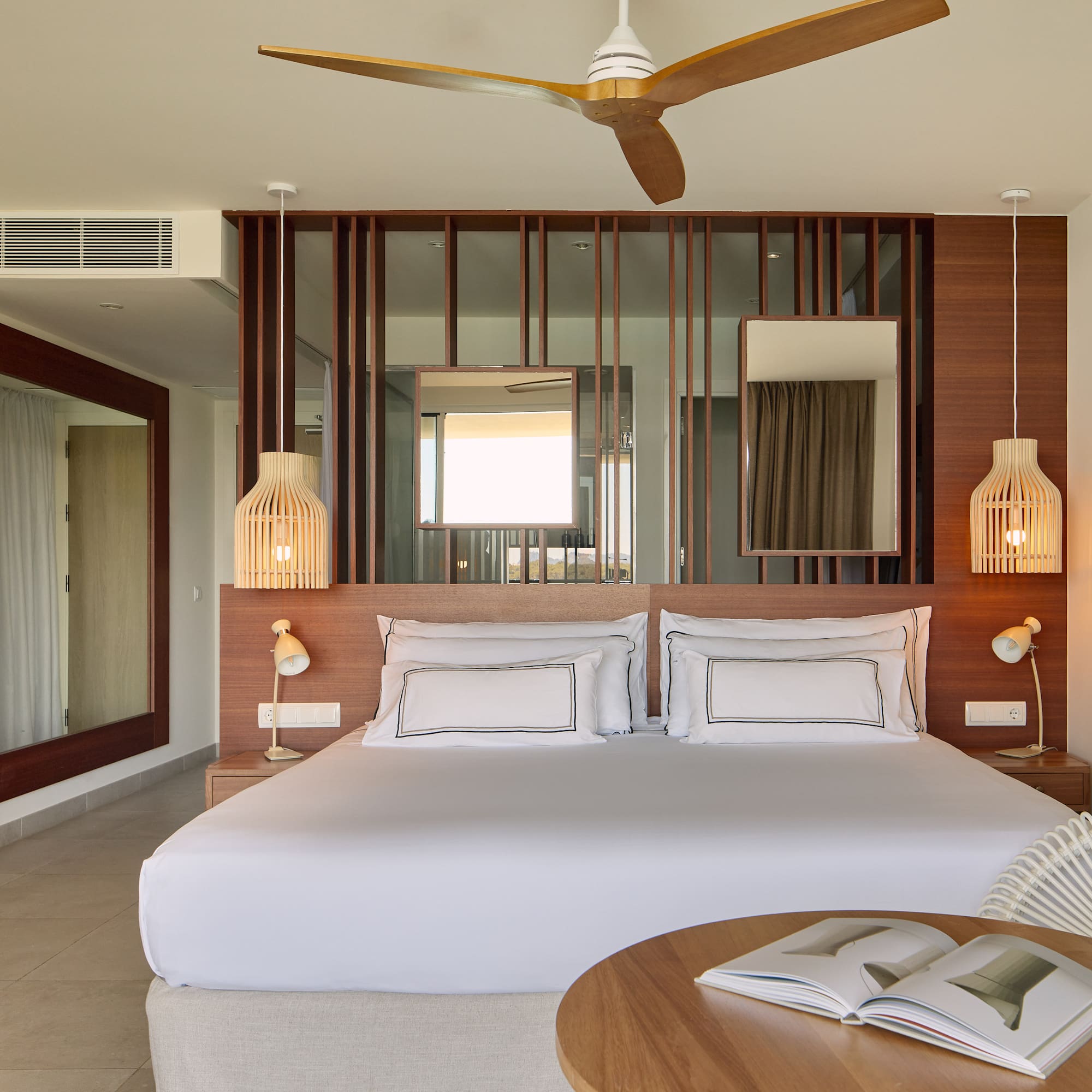 Modern hotel bedroom with king bed, wooden decor, ceiling fan, and rattan chair.