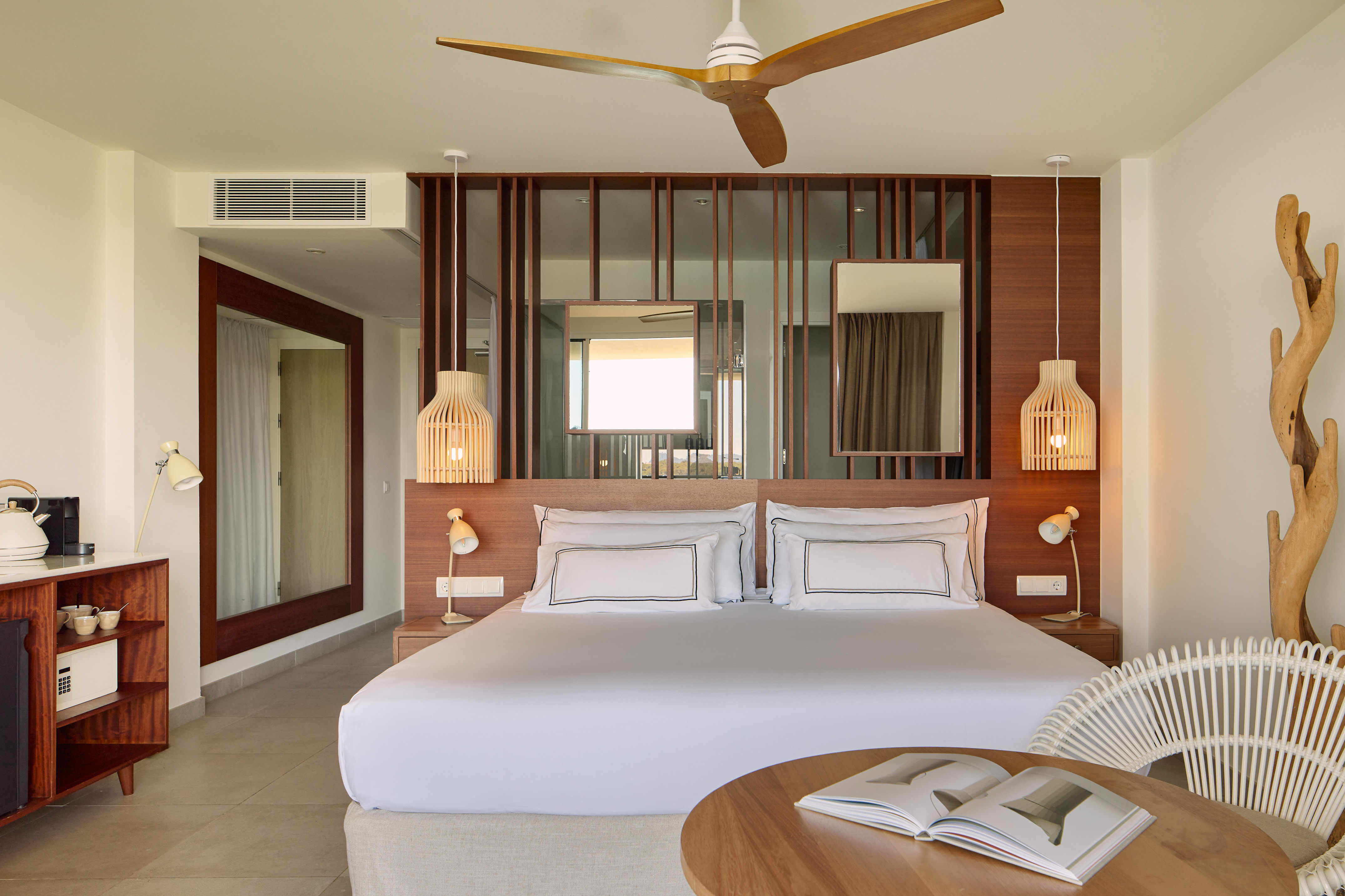 Modern hotel bedroom with king bed, wooden decor, ceiling fan, and rattan chair.
