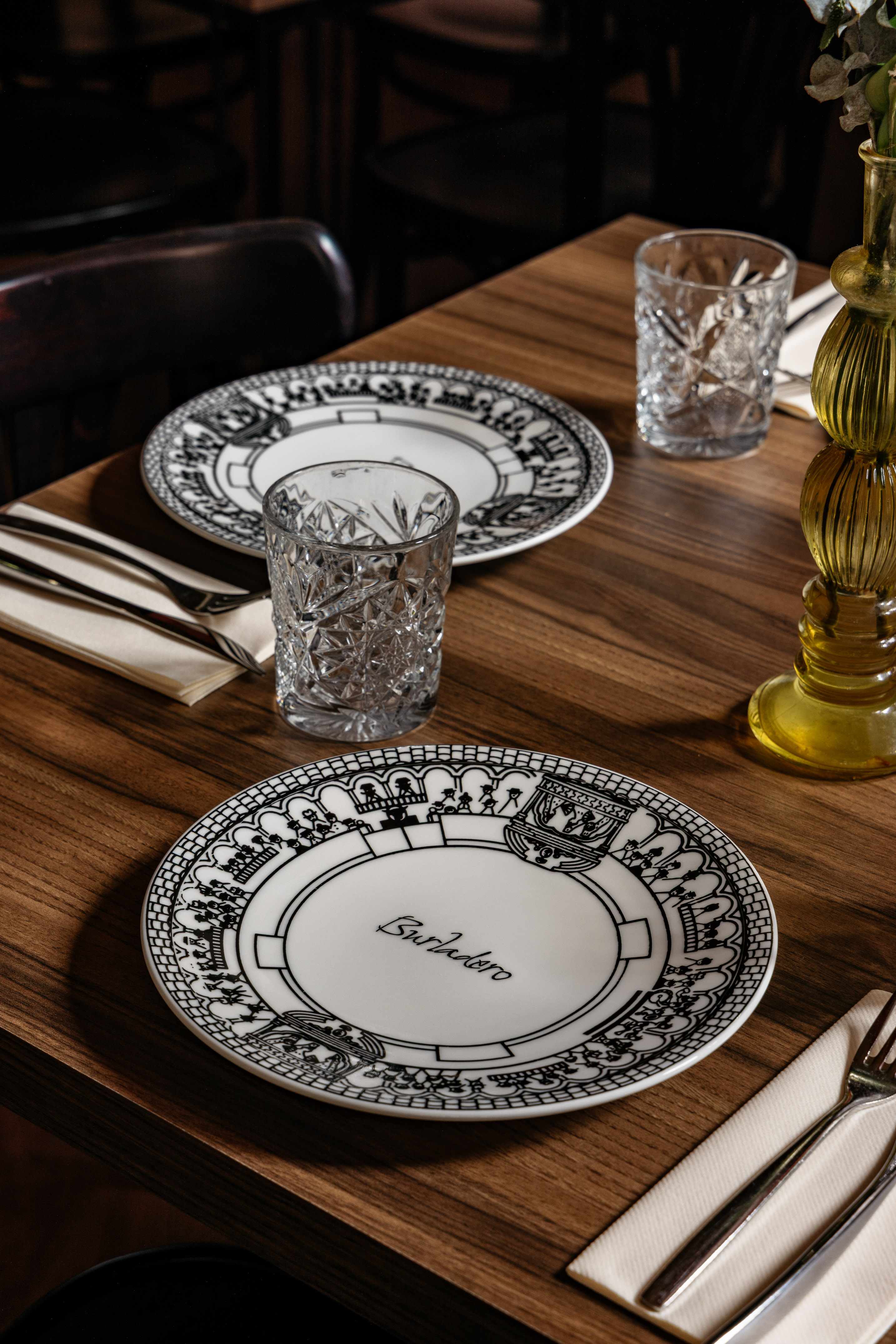 Mesa de restaurante con platos Burladero, vasos de cristal y cubiertos.