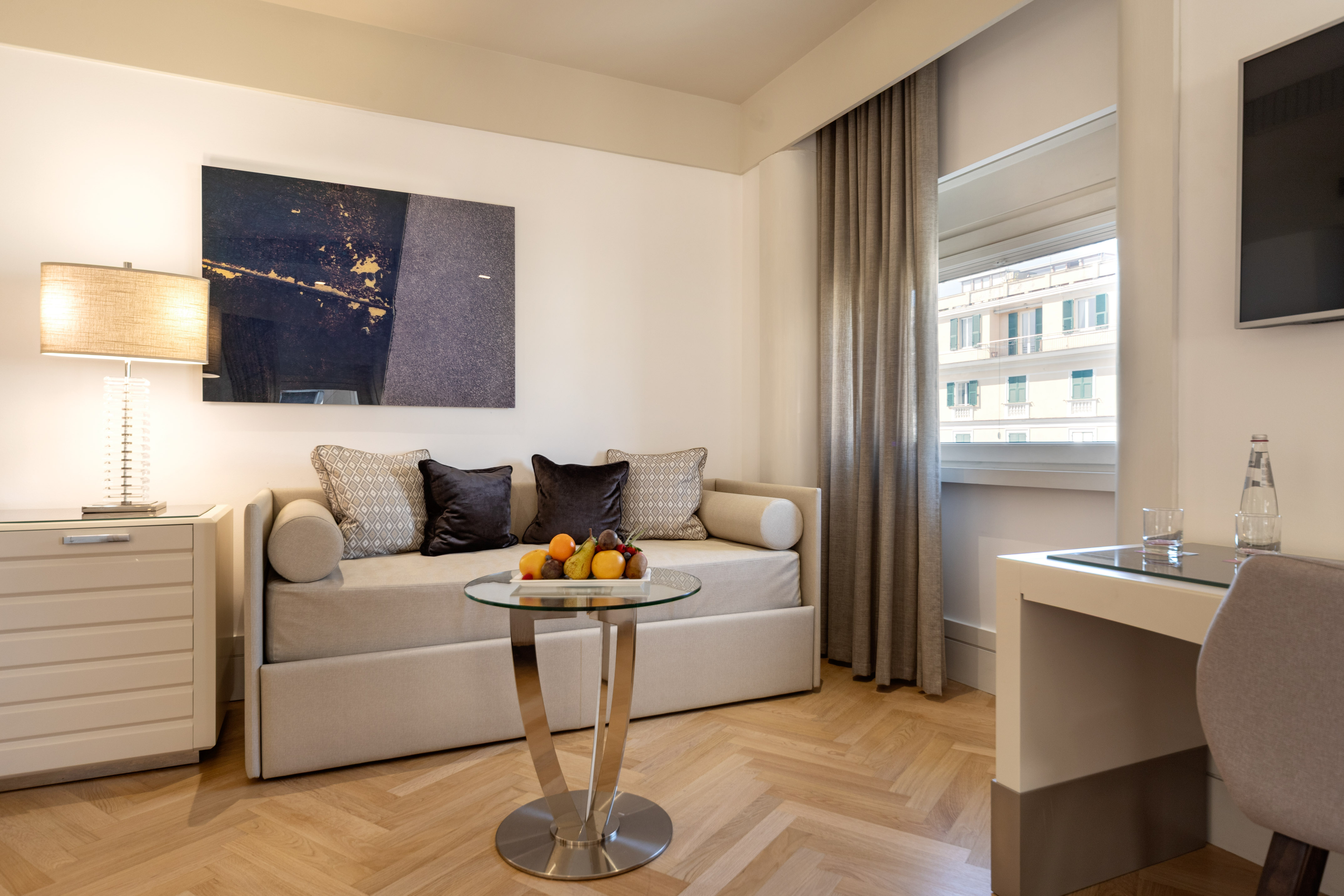 Modern hotel suite living area with daybed, abstract art, and hardwood floor.