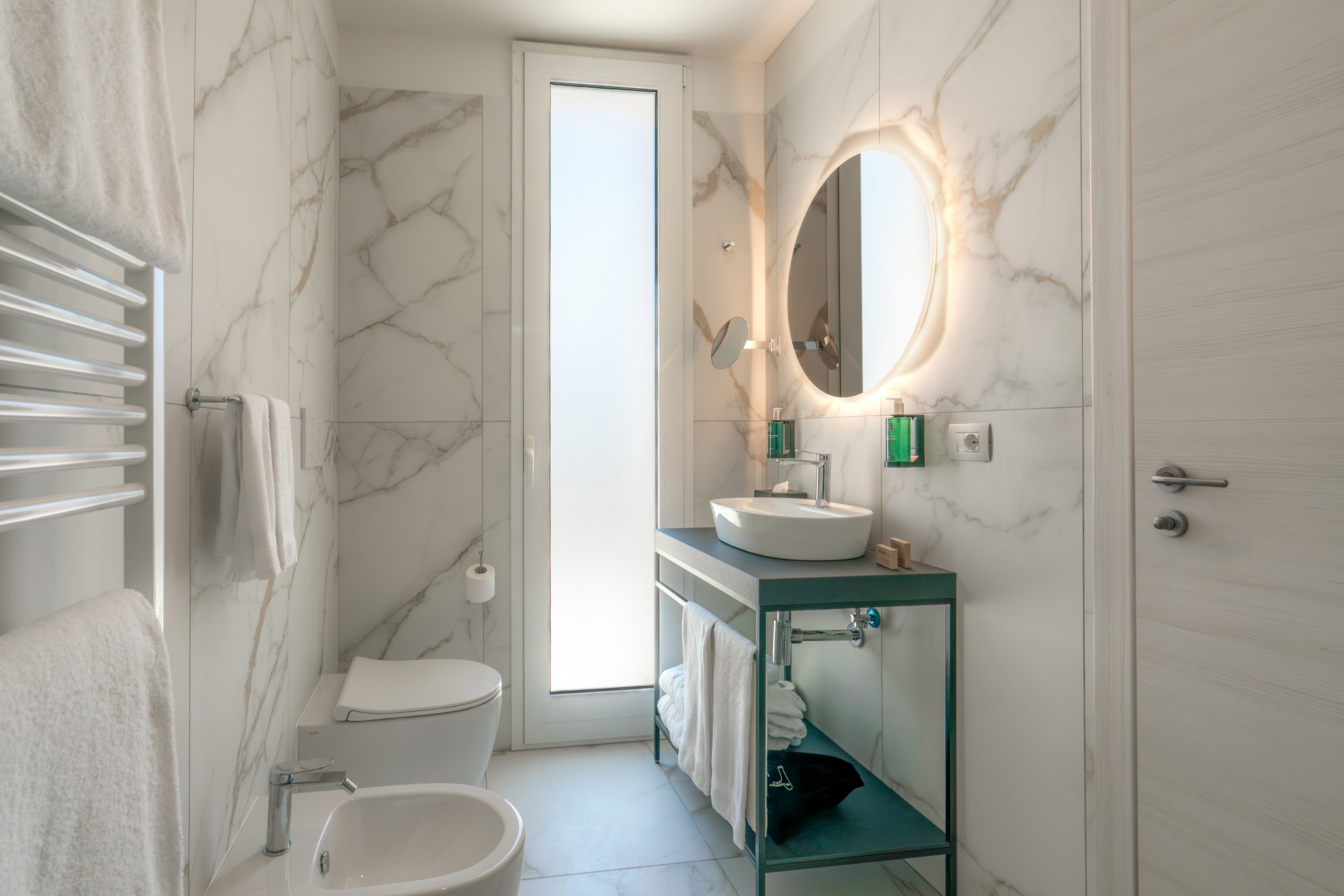 Modern marble bathroom with backlit mirror, floating vanity, toilet, and bidet.