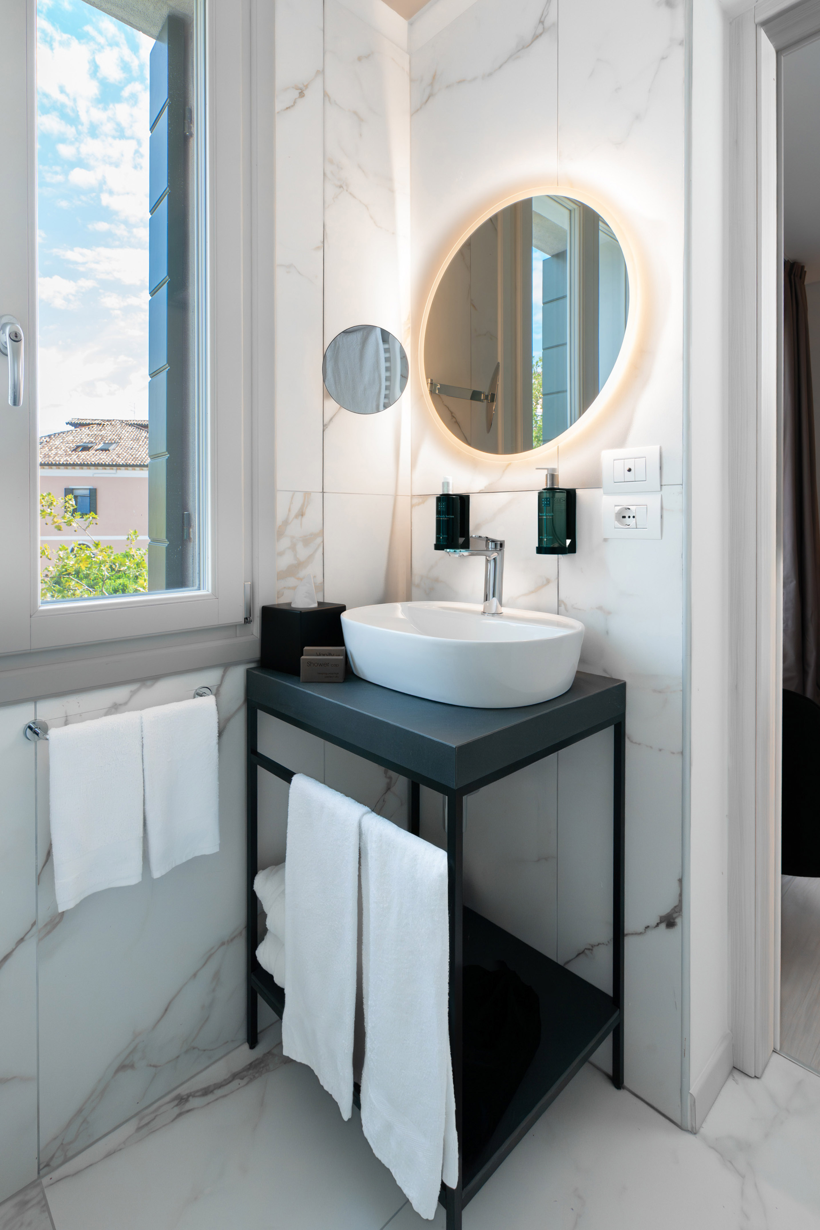White marble bathroom vanity with vessel sink, illuminated mirror, and window.