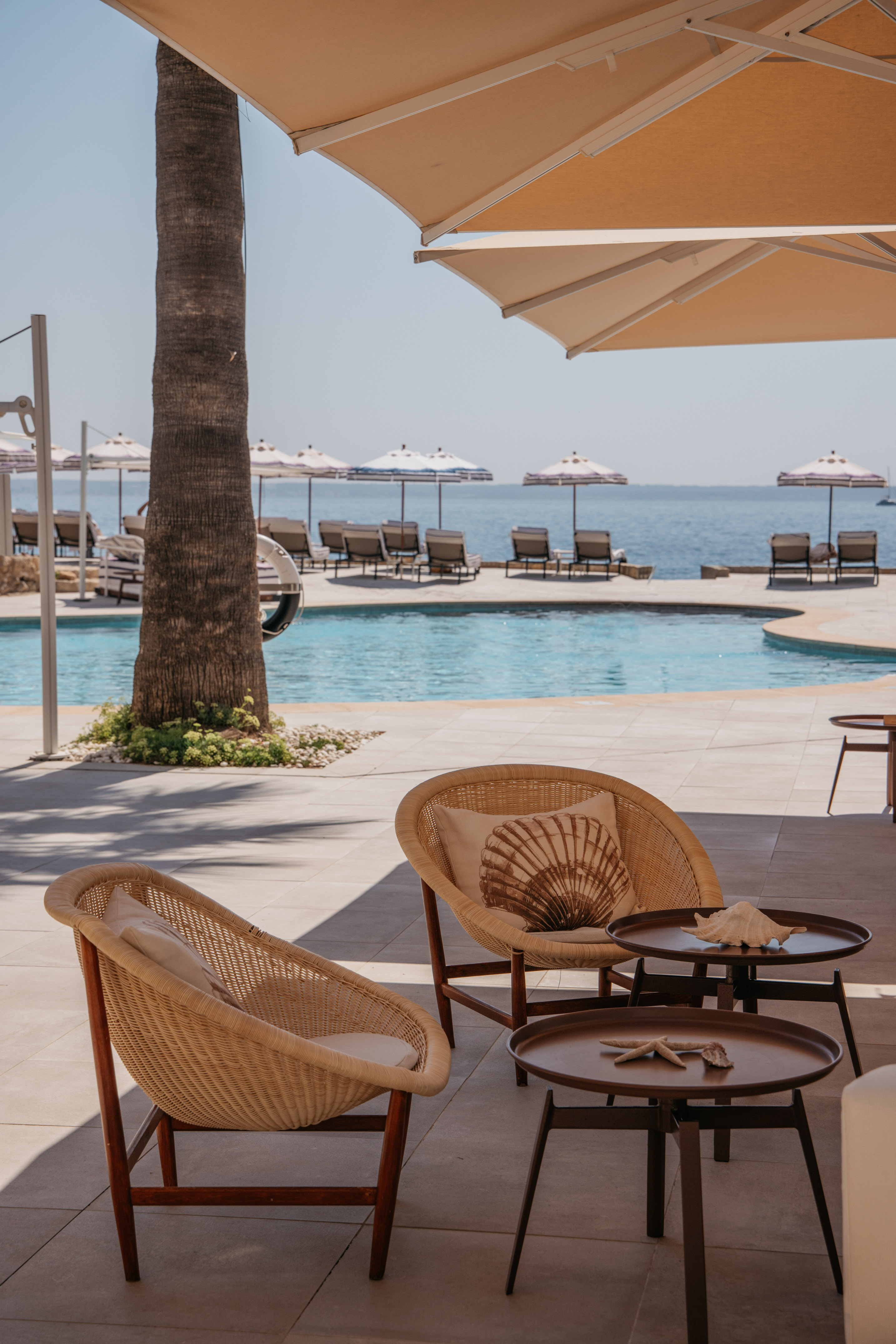 Luxury resort poolside lounge with wicker chairs, ocean view, and beach umbrellas.