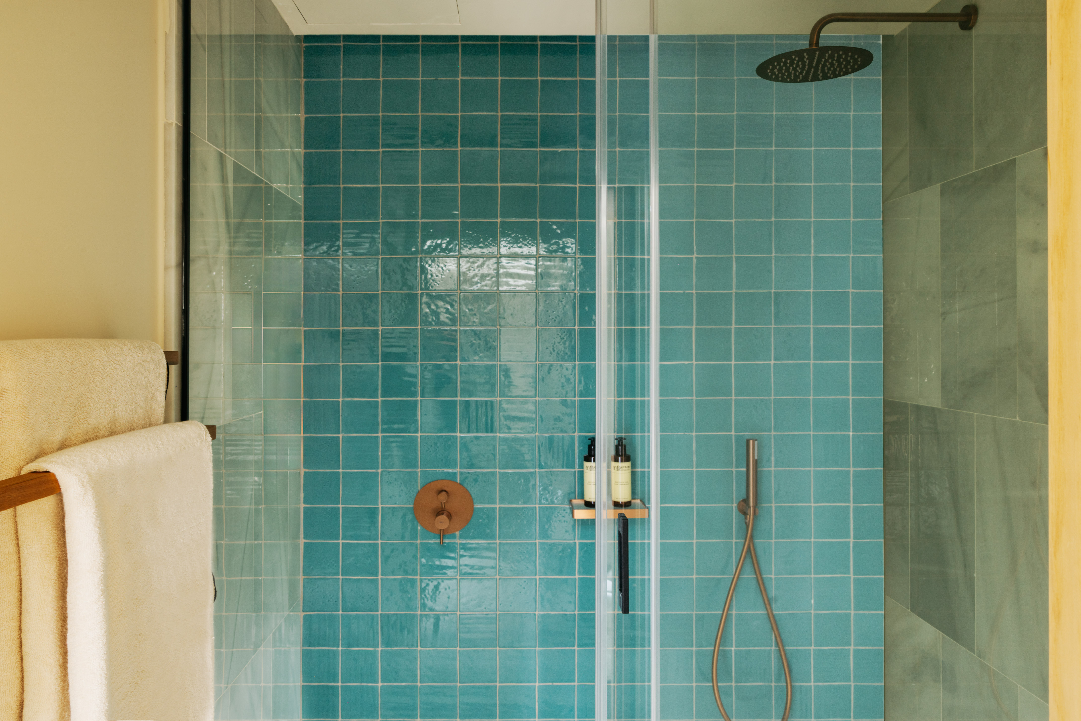 Teal tiled shower with glass screen, modern bronze rainfall showerhead.