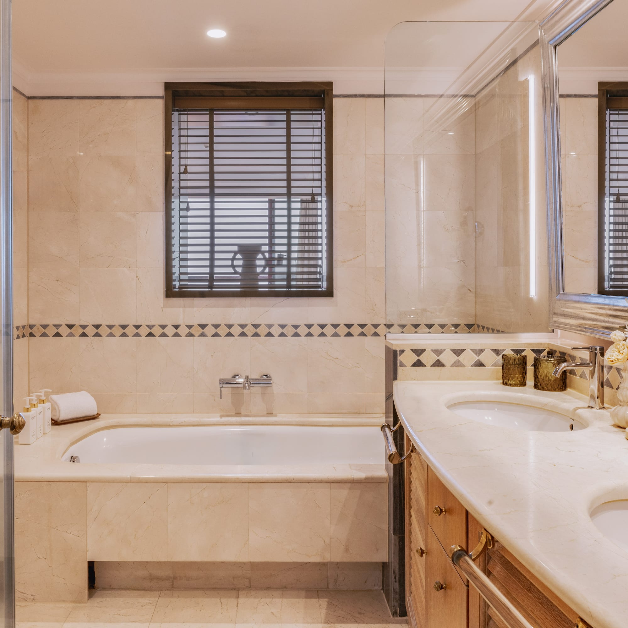 Luxury hotel bathroom with marble walls, bathtub, and double vanity.