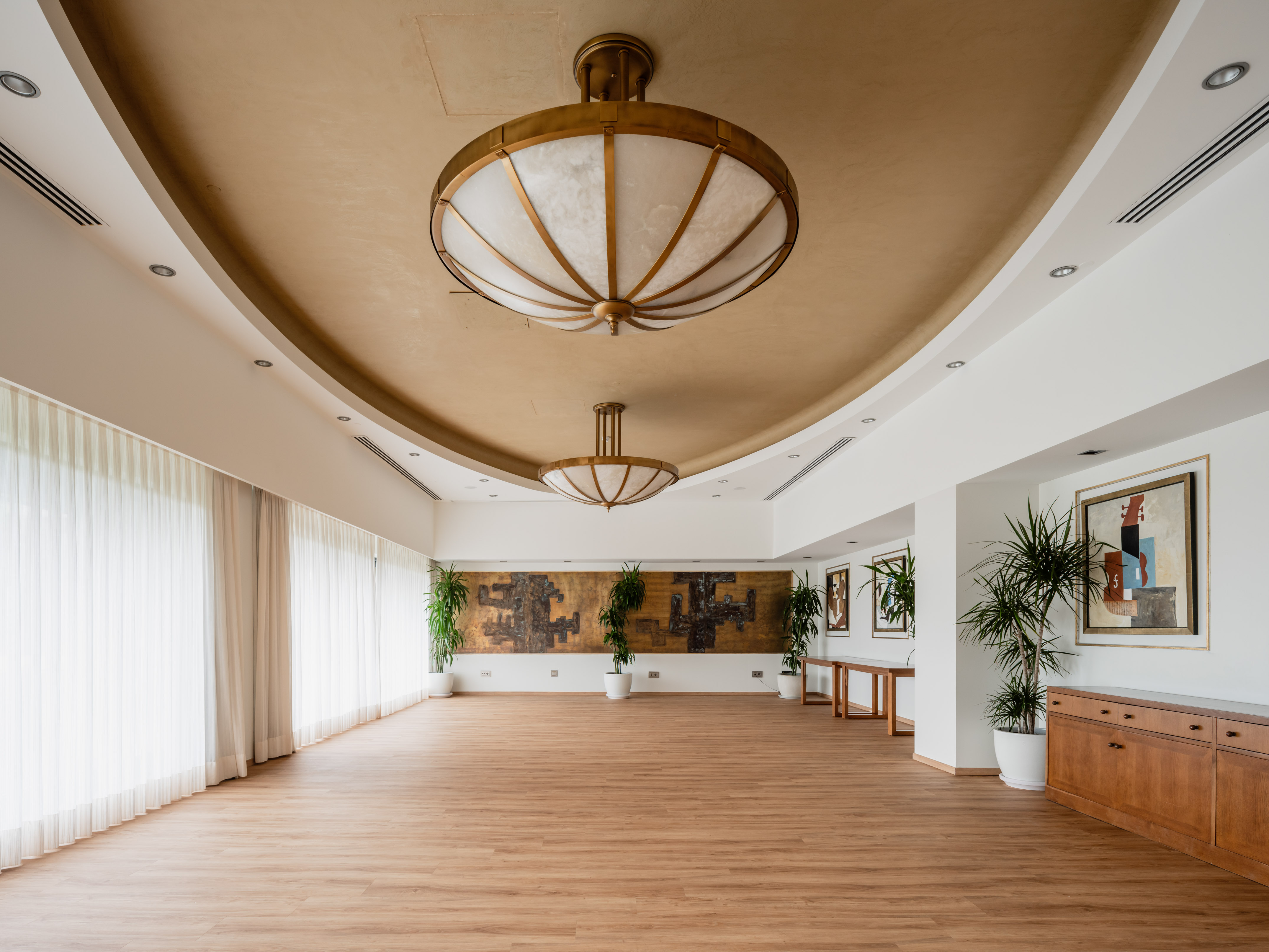 Spacious modern event hall with ornate ceiling lights and wood floor.