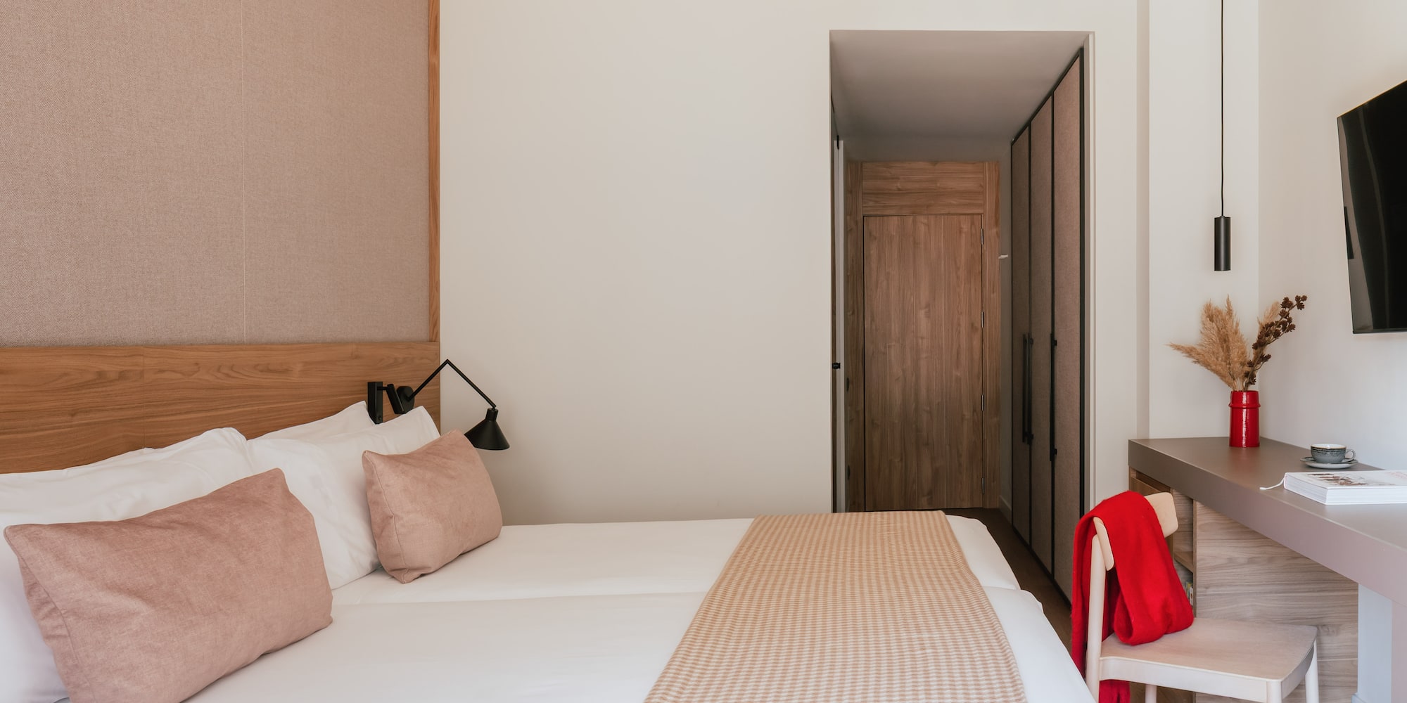 Modern hotel bedroom with clean white bed, pink accents, and wooden closet.