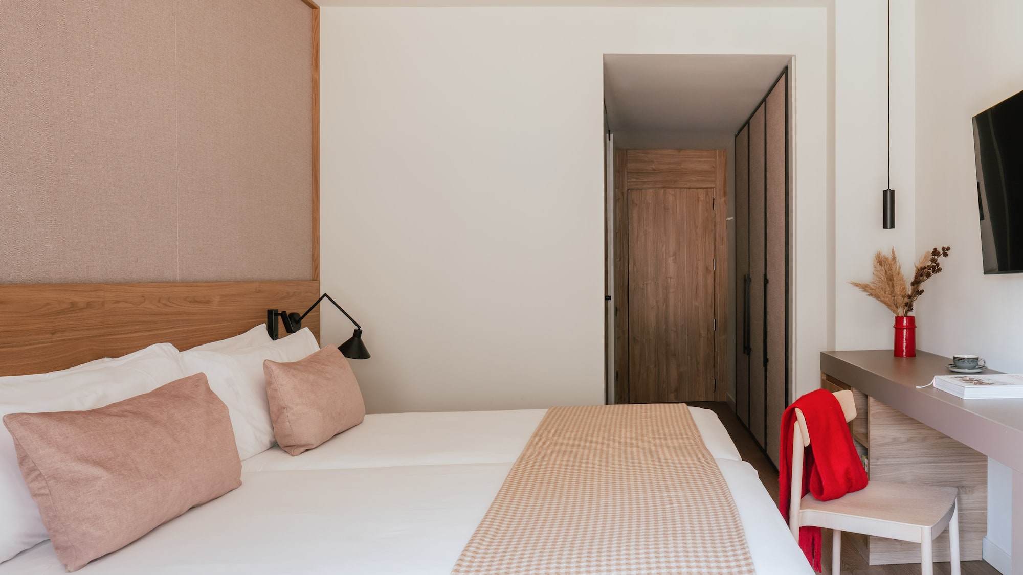 Modern hotel bedroom with clean white bed, pink accents, and wooden closet.