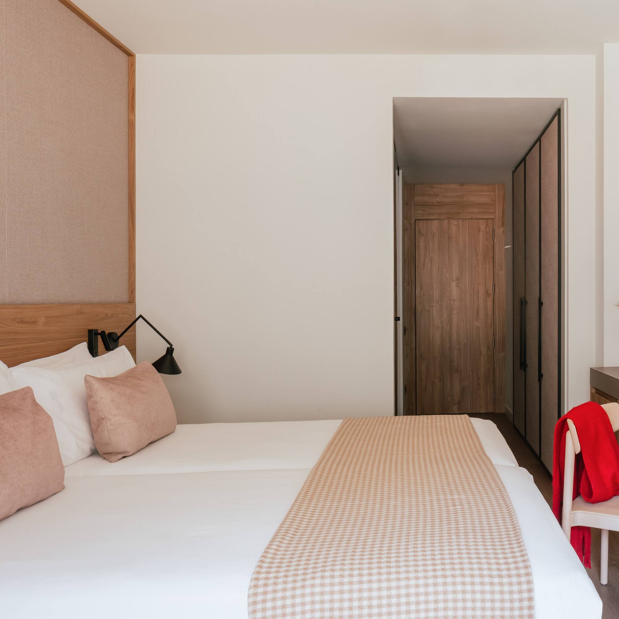 Modern hotel bedroom with clean white bed, pink accents, and wooden closet.