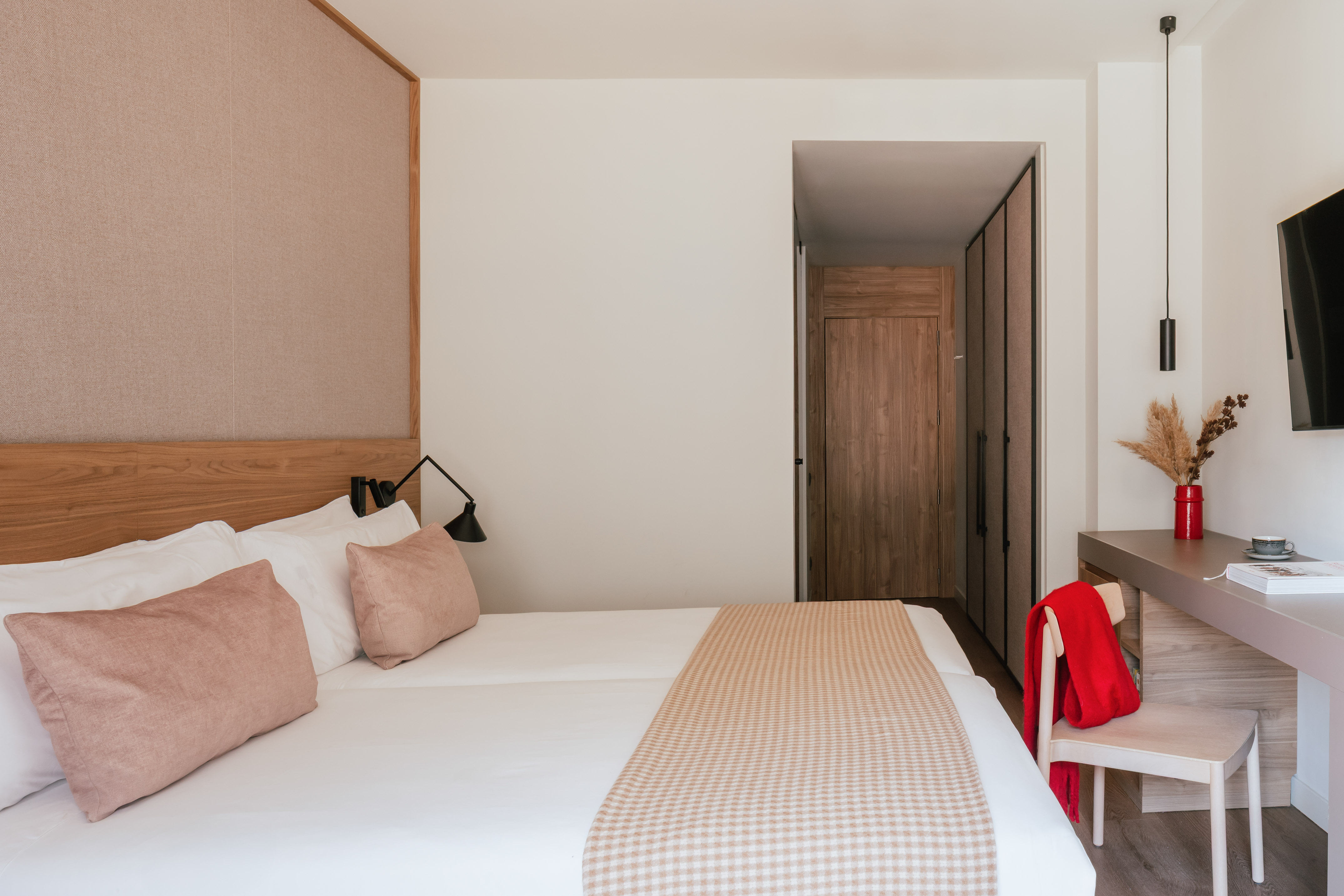 Modern hotel bedroom with clean white bed, pink accents, and wooden closet.