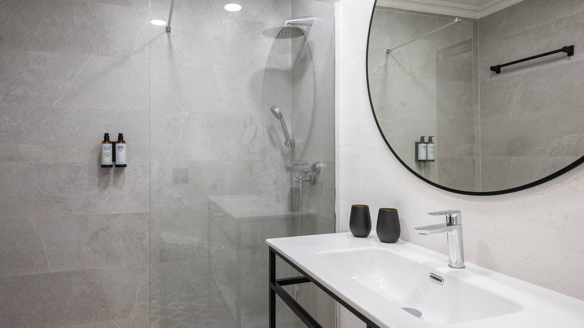 Contemporary bathroom with grey tiles, walk-in shower, vanity, and round mirror.