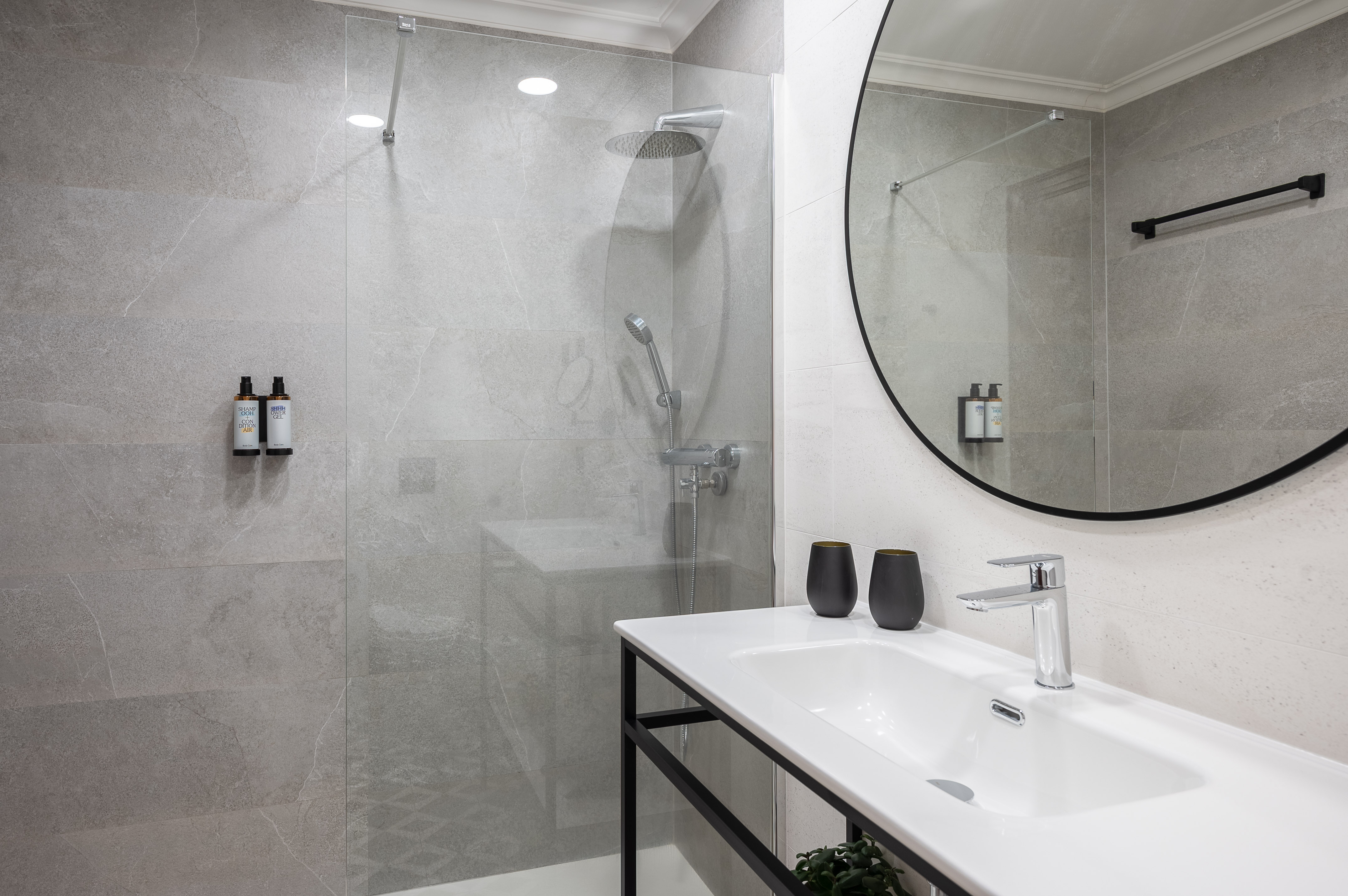 Contemporary bathroom with grey tiles, walk-in shower, vanity, and round mirror.