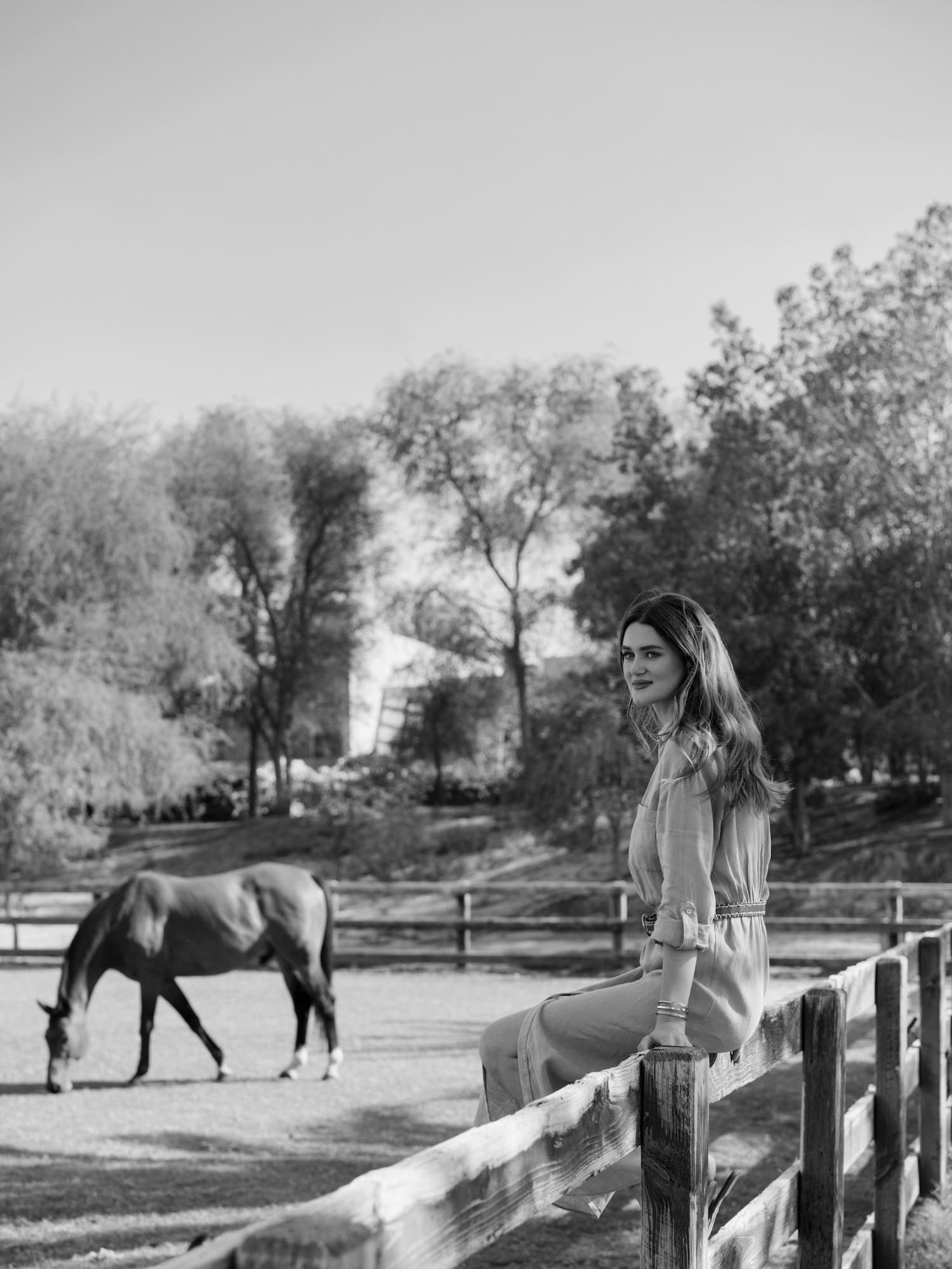 a woman sitting on a fence with a horse in the background