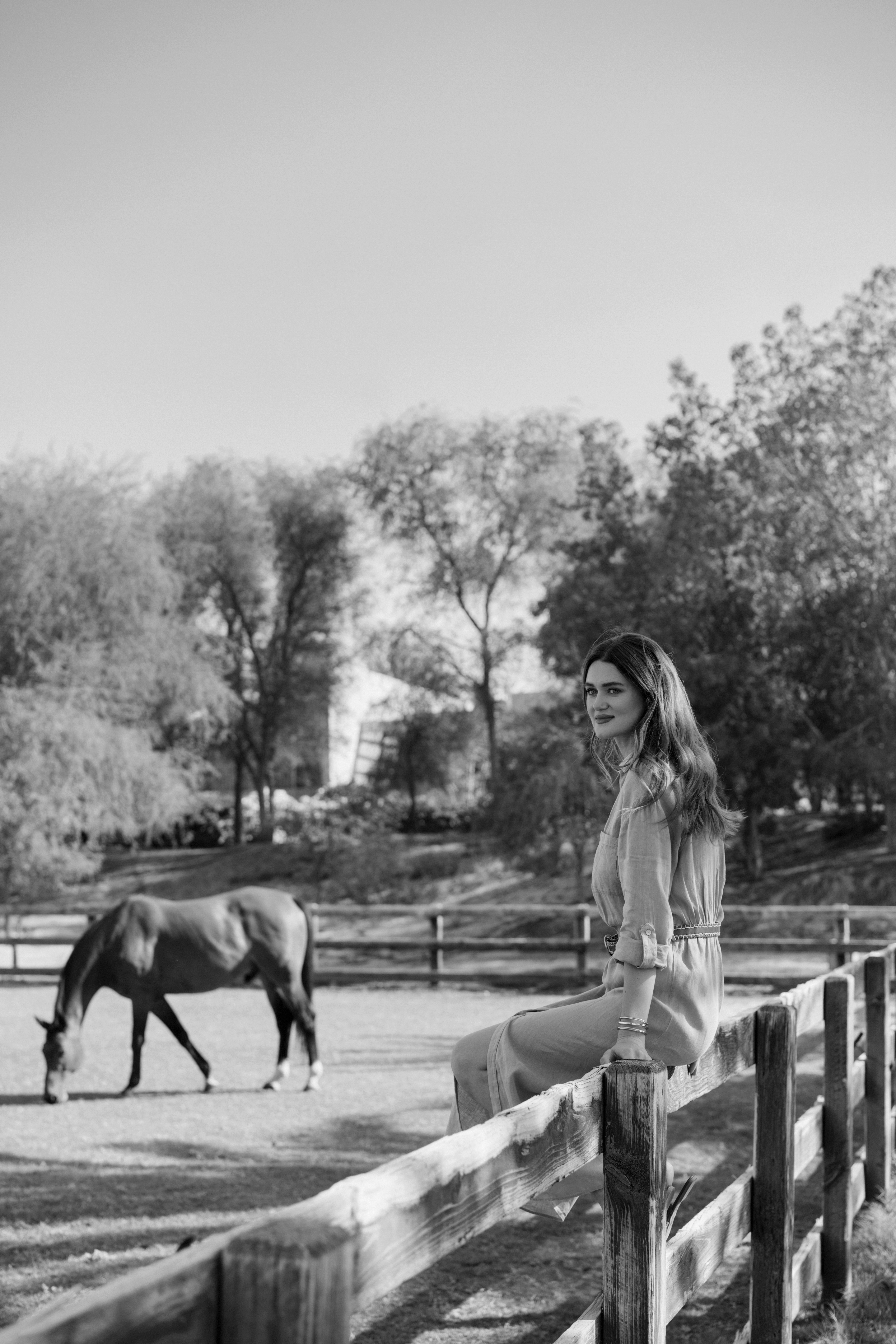 a woman sitting on a fence with a horse in the background