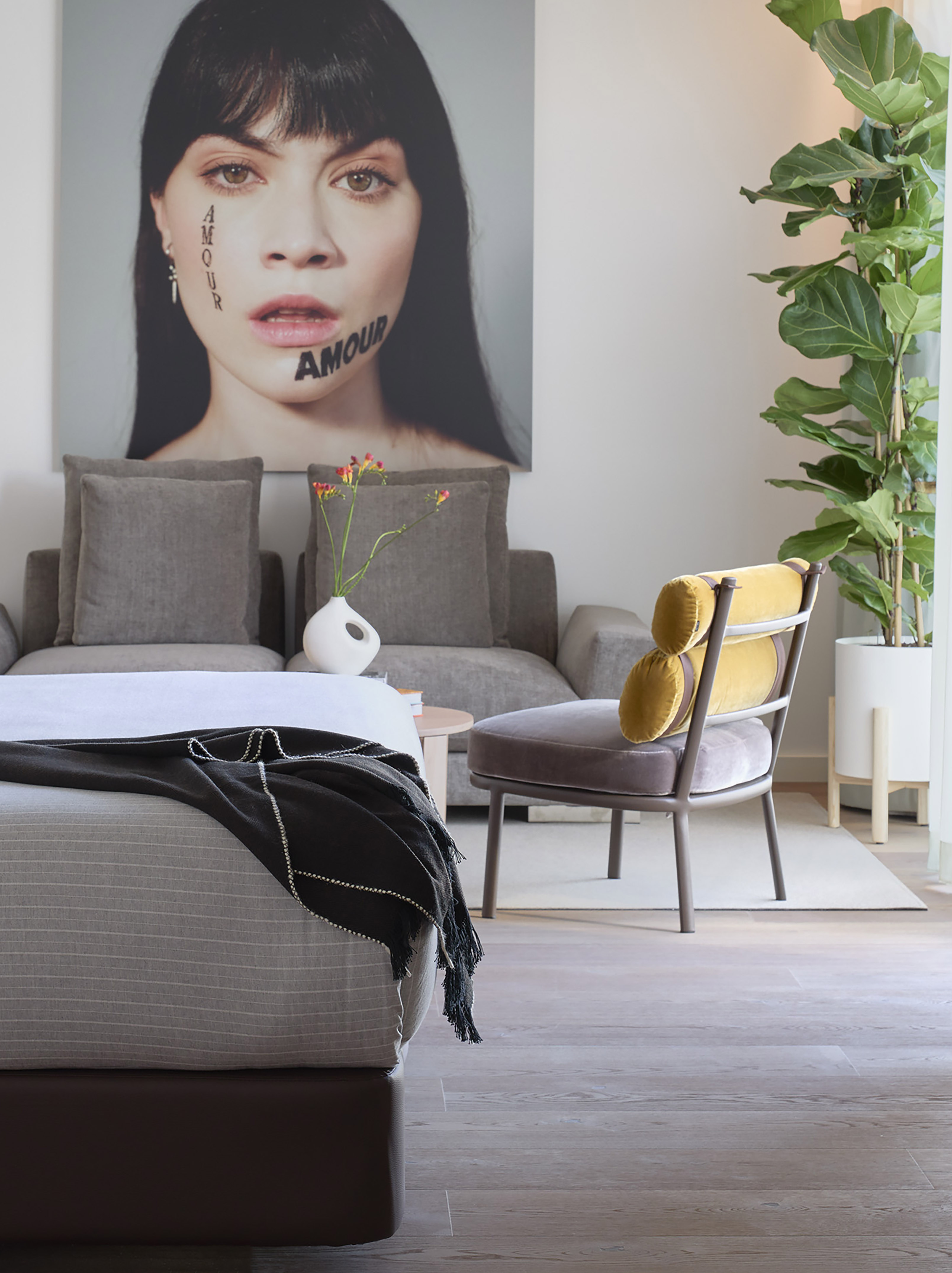 Modern room with 'Amour' portrait, bed, grey sofa, and yellow accent chair.