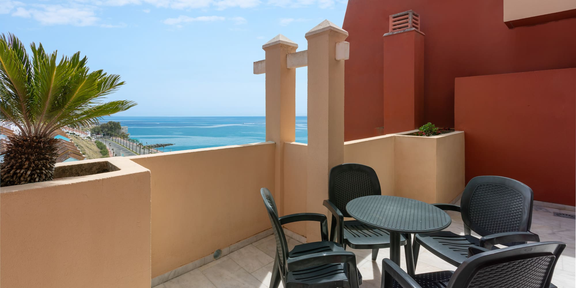 Coastal balcony with ocean view, palm tree, and outdoor dining set.
