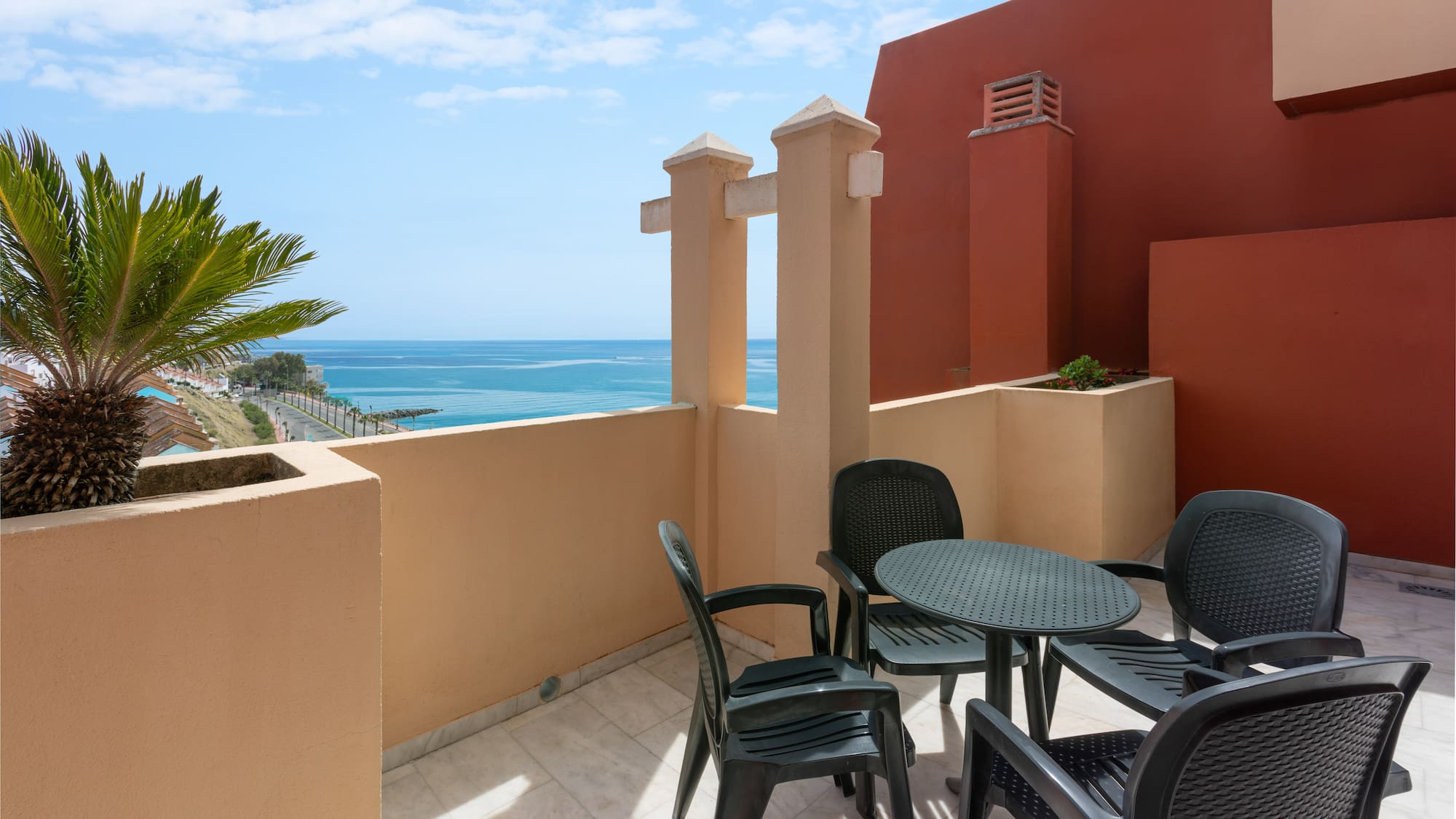 Coastal balcony with ocean view, palm tree, and outdoor dining set.