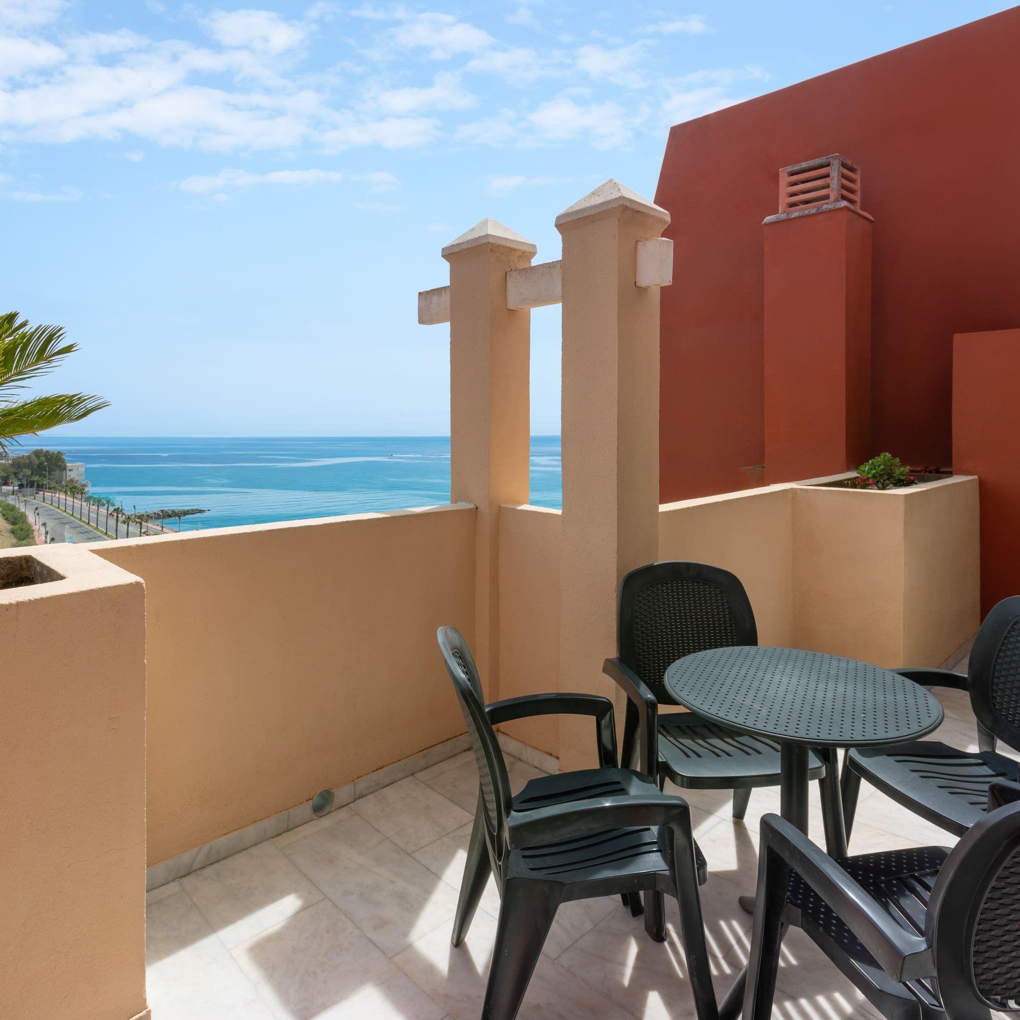 Coastal balcony with ocean view, palm tree, and outdoor dining set.
