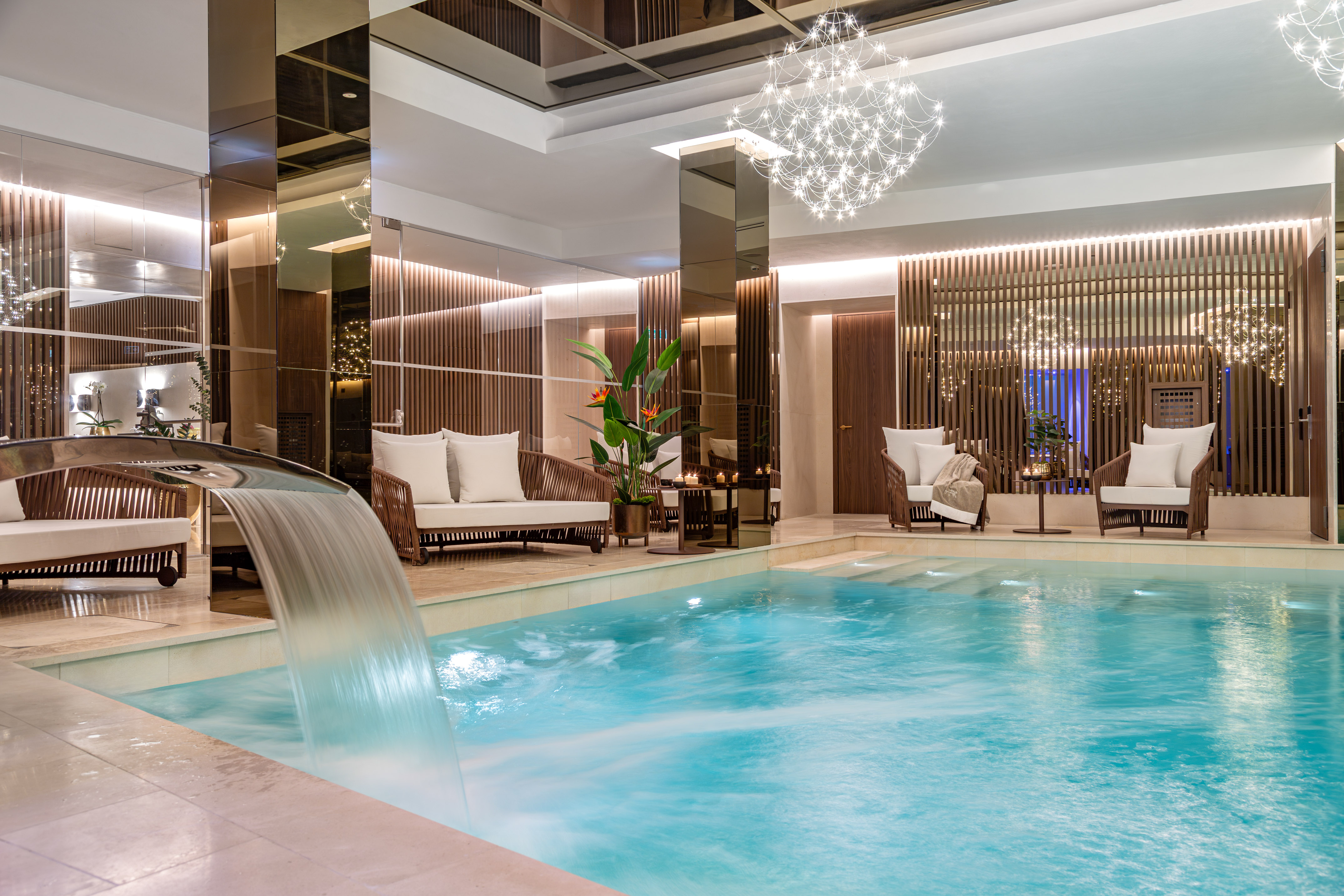 Elegant indoor spa pool with waterfall, modern lounge seating, and ambient lighting.
