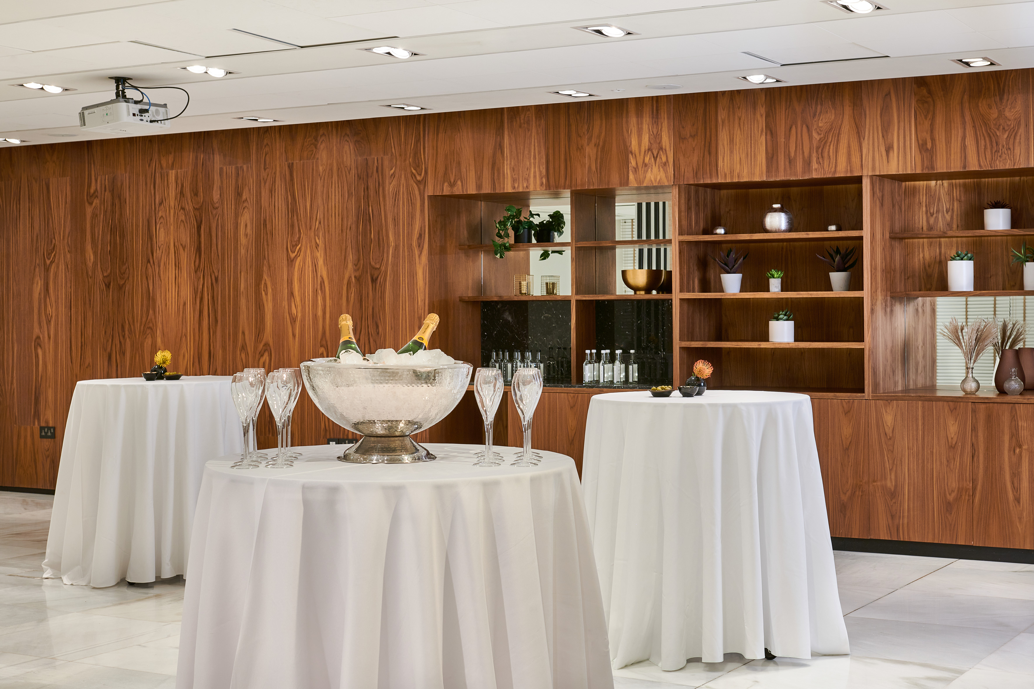 Modern event space with champagne service, white tables, and wood paneling.
