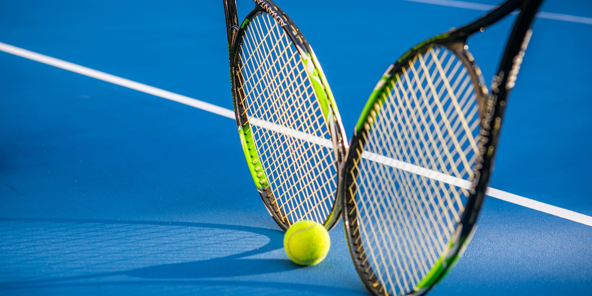 two tennis rackets and a ball on a blue court