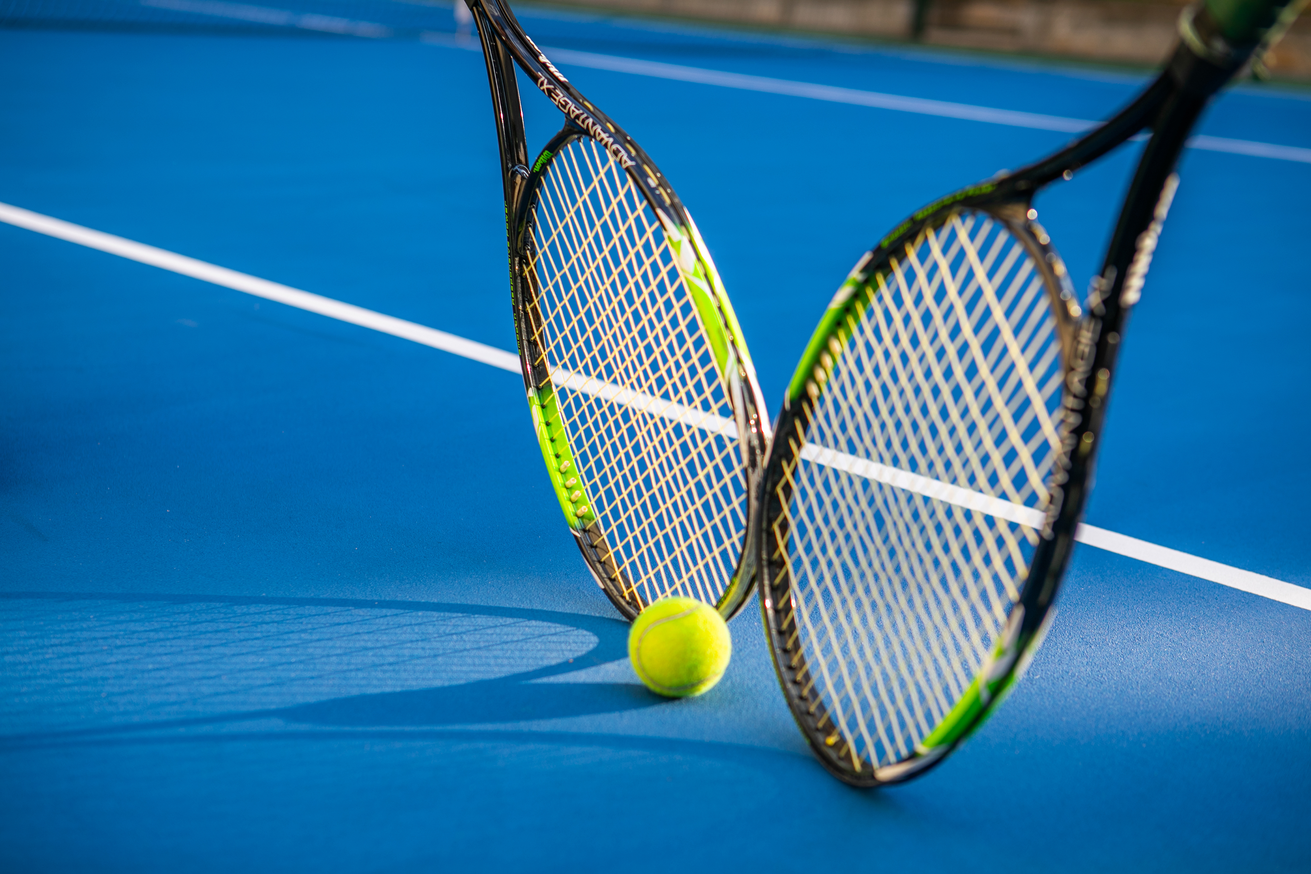 Two black and green tennis rackets with a yellow ball on a blue tennis court.