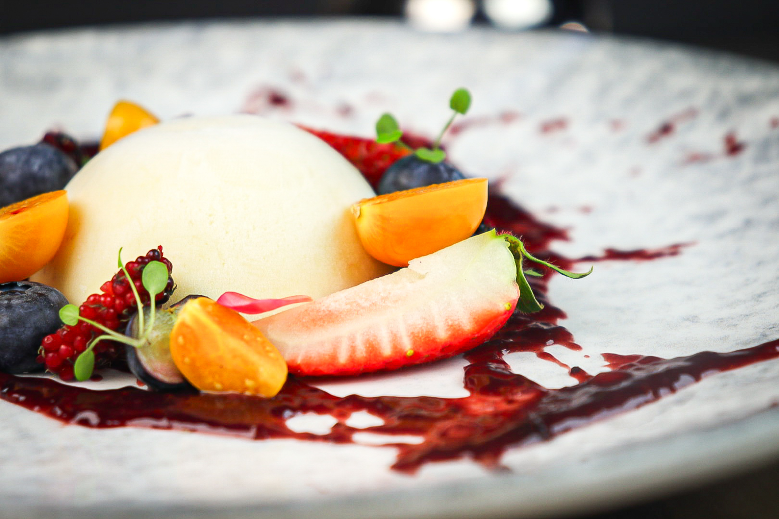 White dome dessert with berries, physalis, strawberry, and fruit coulis.