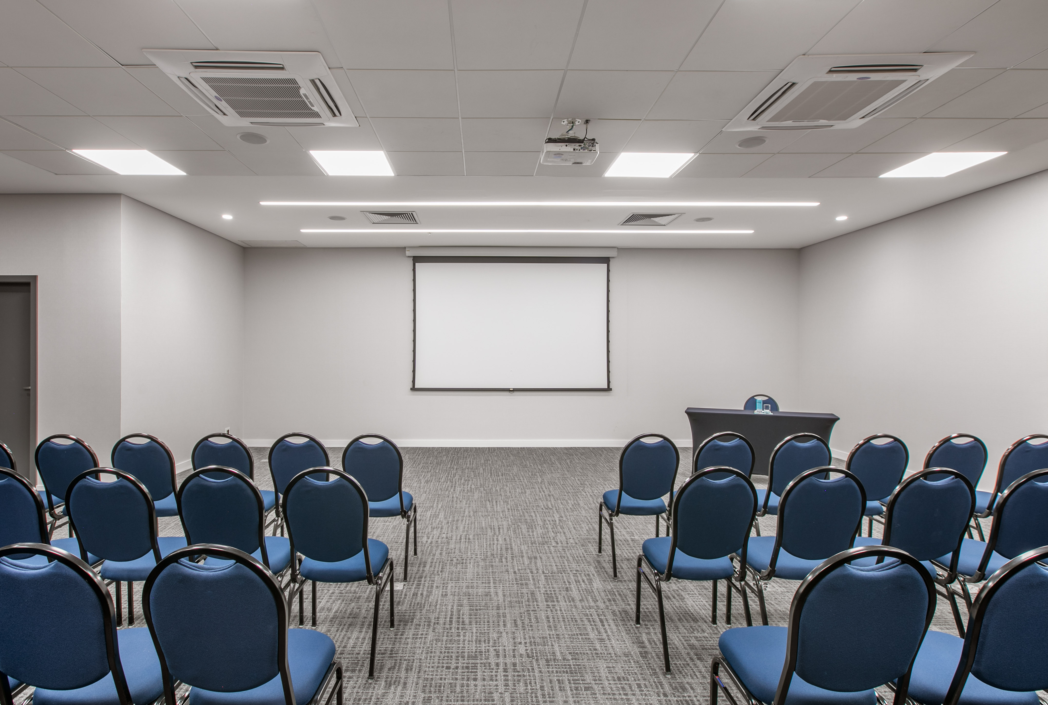 Empty conference room with blue chairs, projector screen, and presentation table.