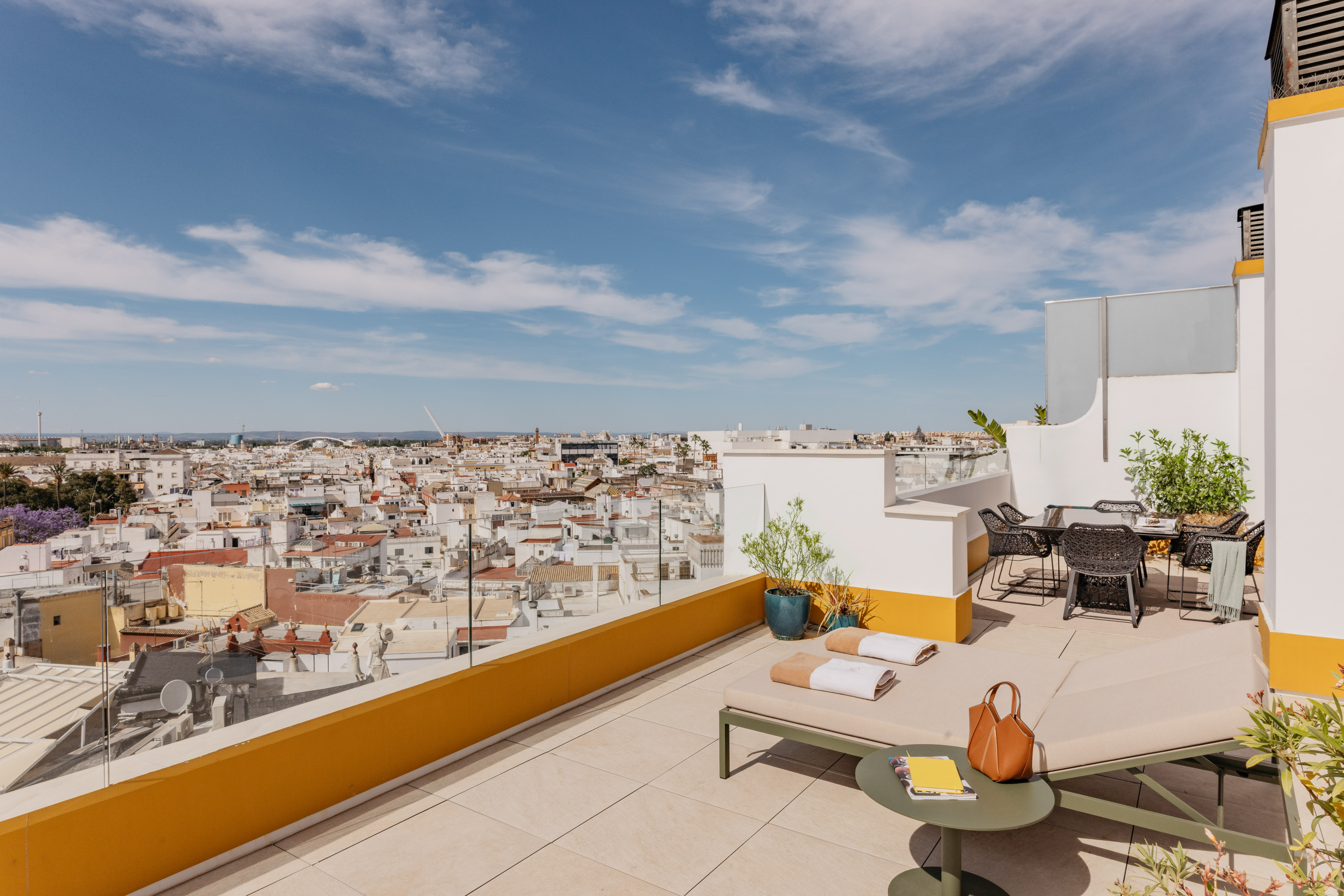 Terraza de azotea con tumbonas y vistas panorámicas a la ciudad de Sevilla.