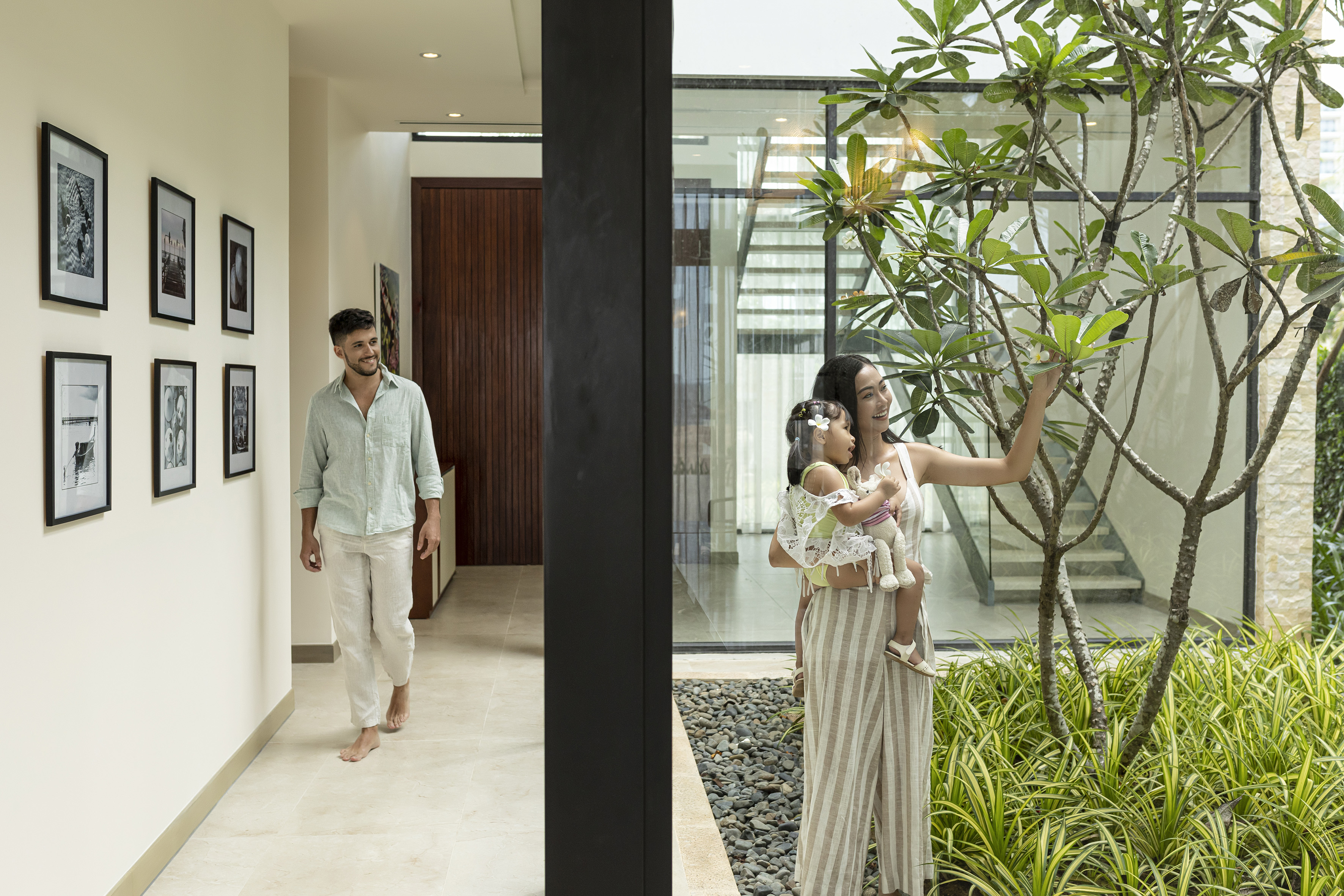 Family in modern home: man walks in hallway, woman and baby by indoor garden.