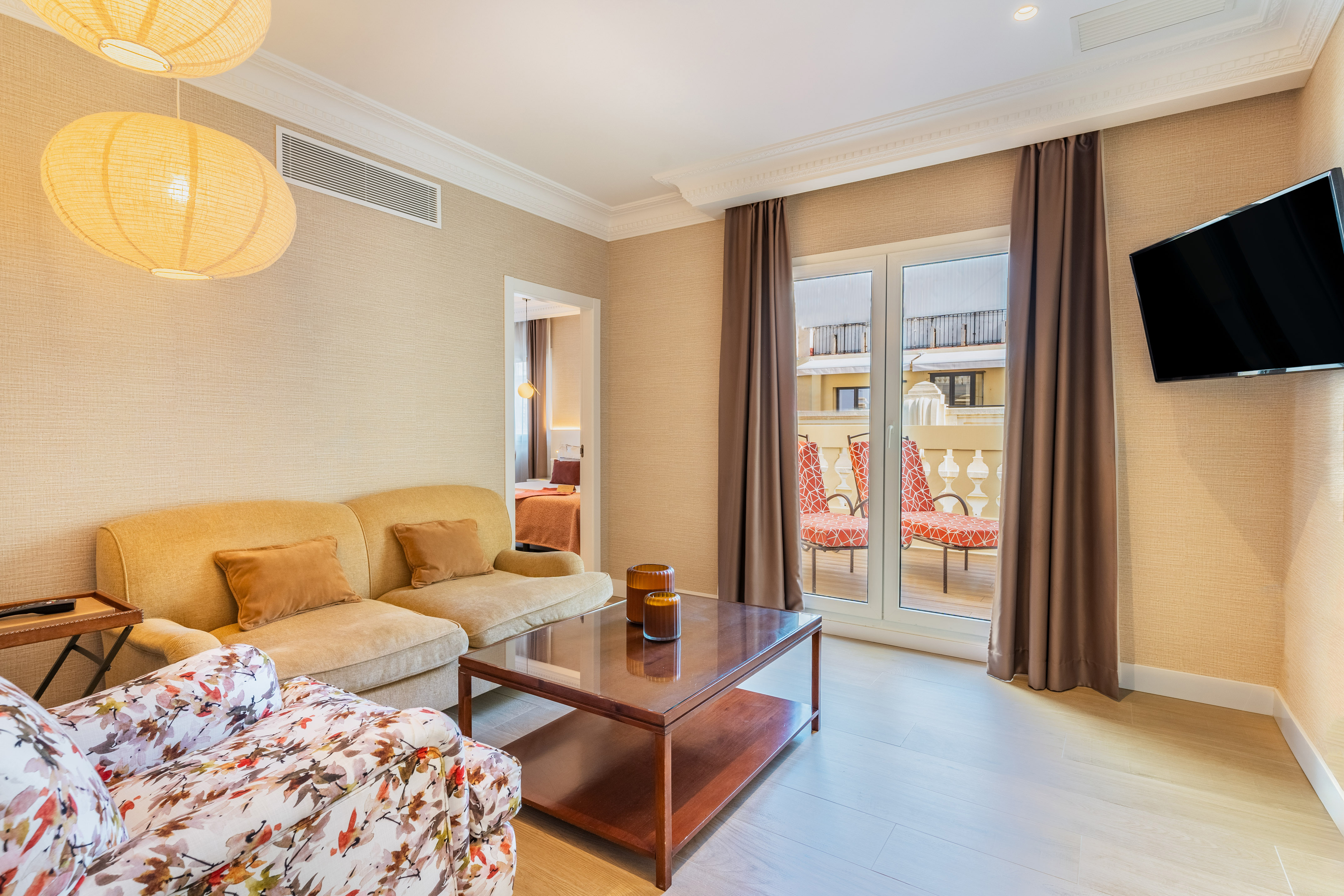 Bright hotel suite living room with sofa, armchair, coffee table, and balcony.