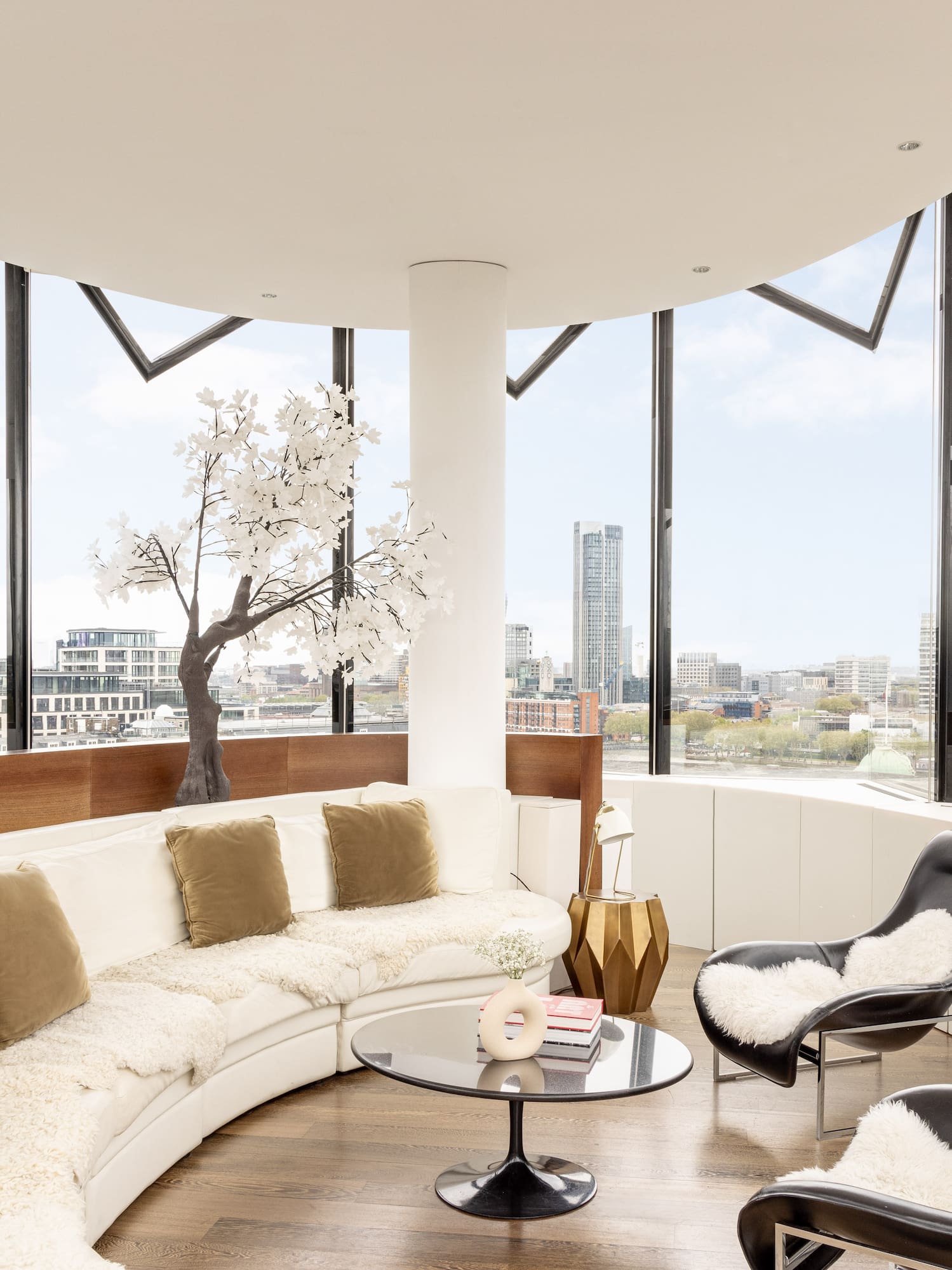 a room with a large round couch and a table with a tree and a window