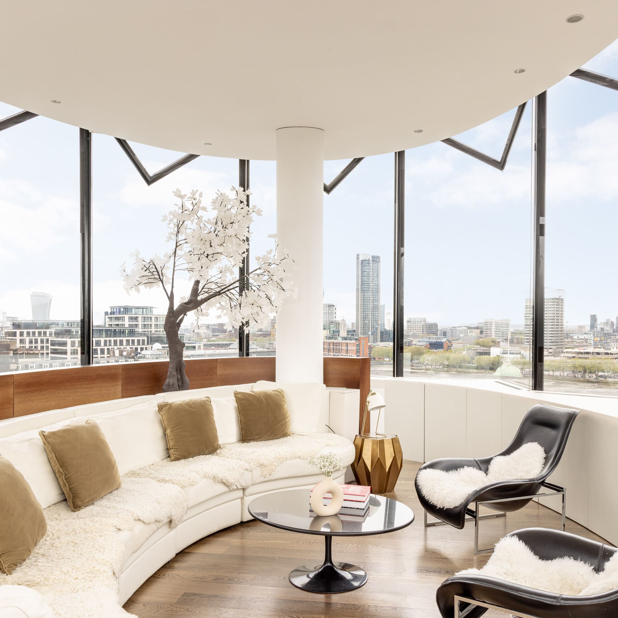 a room with a large round couch and a table with a tree and a window