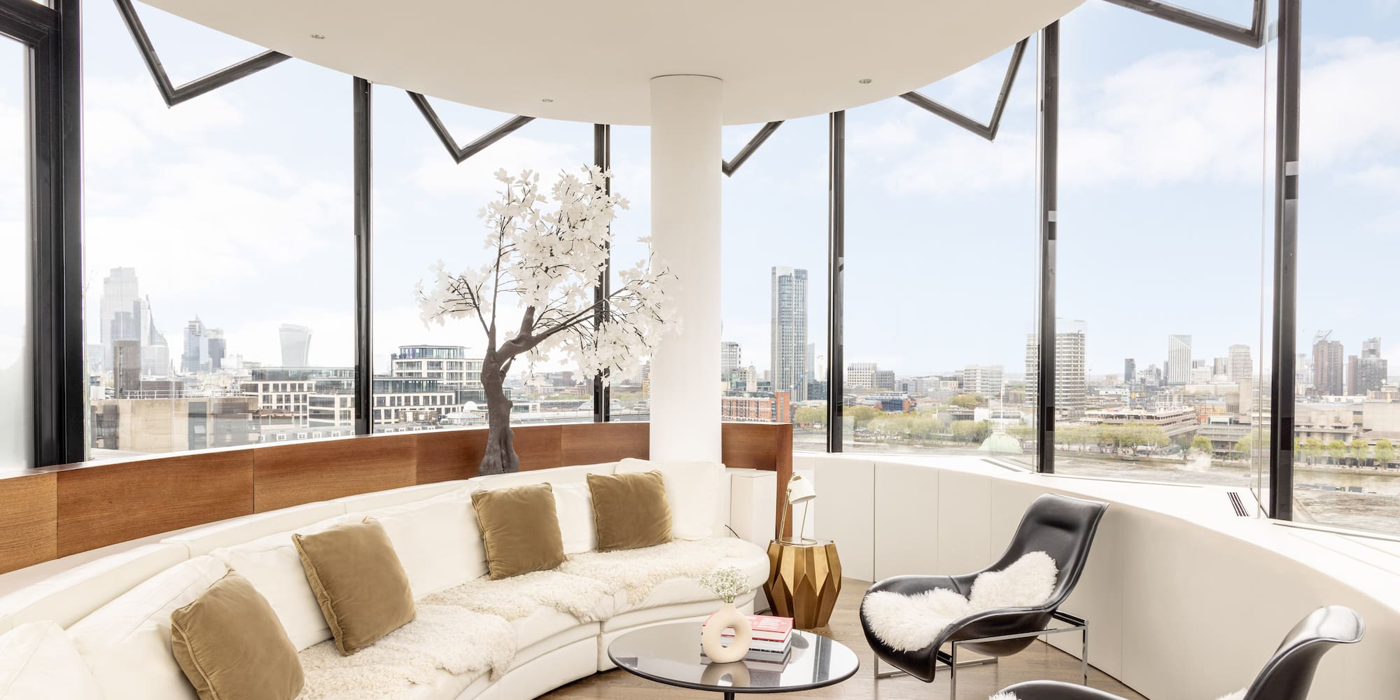 a room with a large round couch and a table with a tree and a window