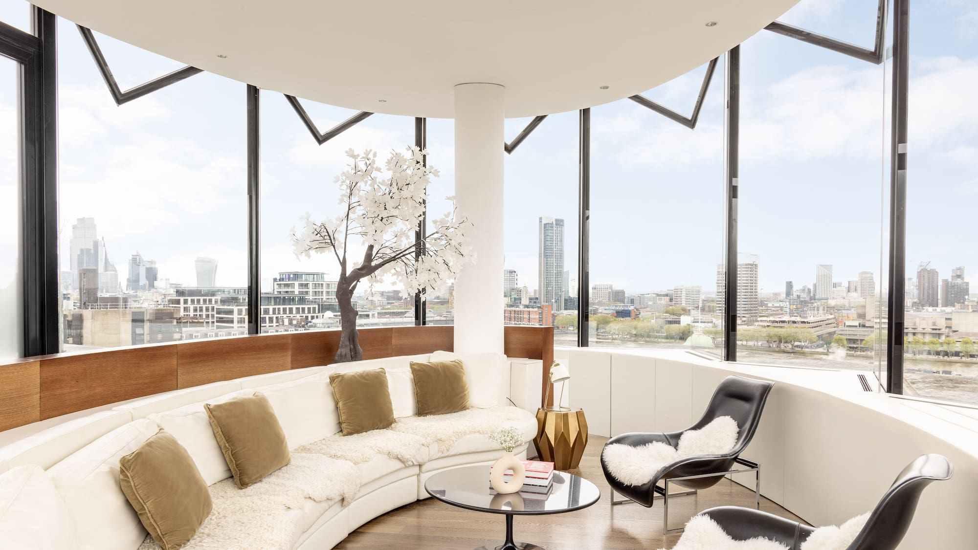 a room with a large round couch and a table with a tree and a window
