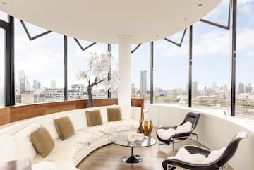 a room with a large round couch and a table with a tree and a window