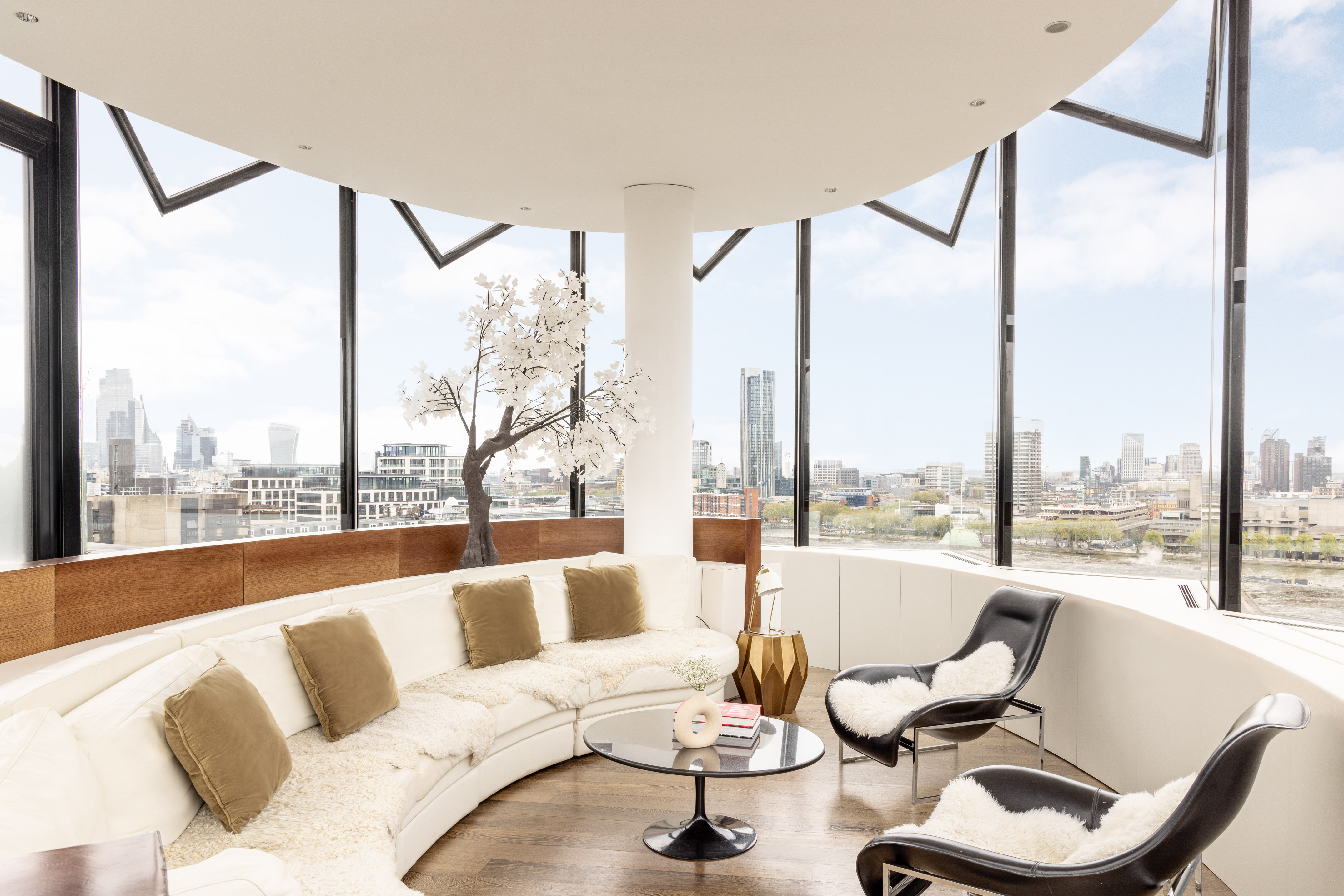 Luxury living room with panoramic city view, curved sofa, and modern chairs.
