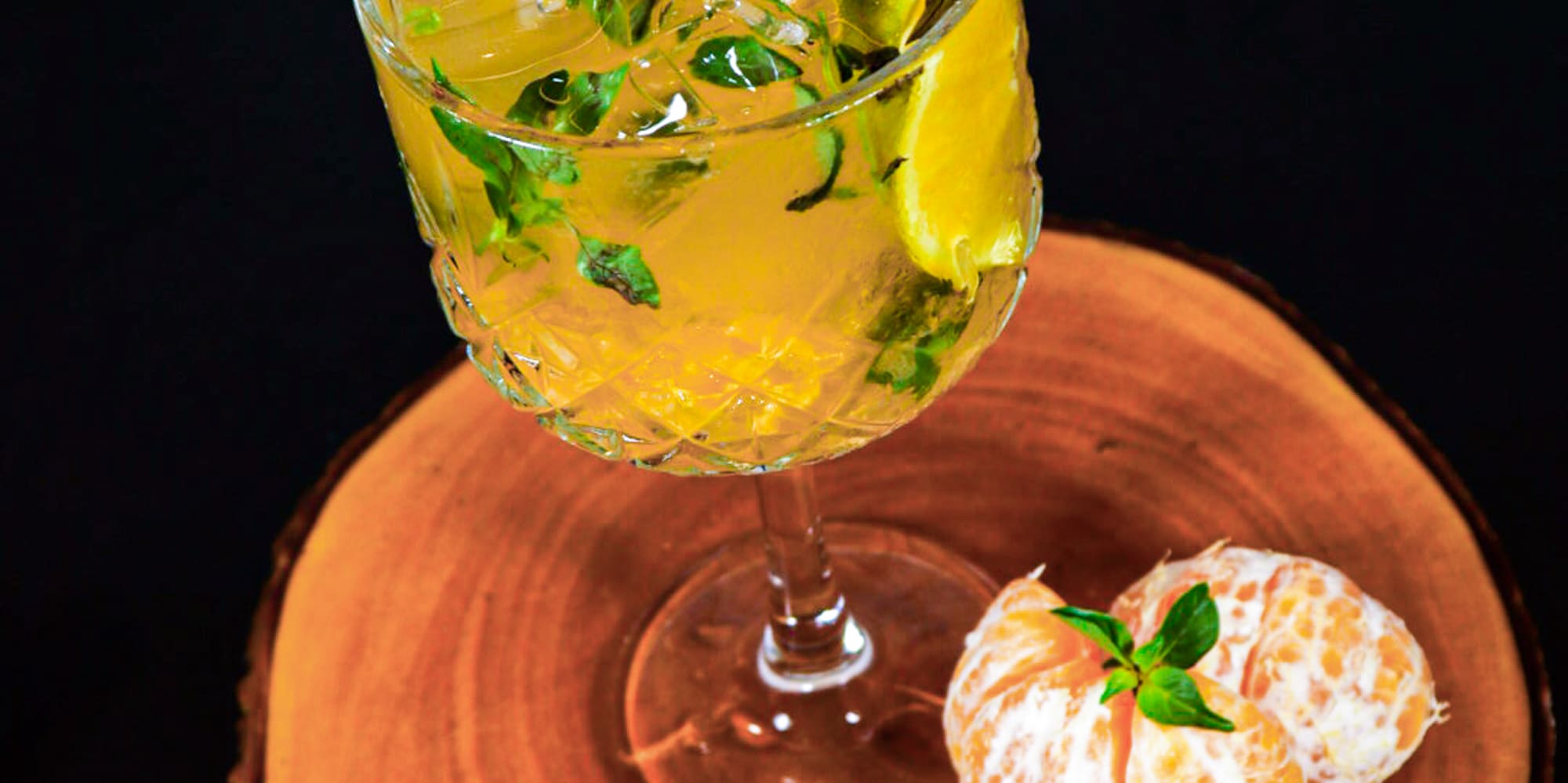 a glass of liquid with ice and mint on a wood surface
