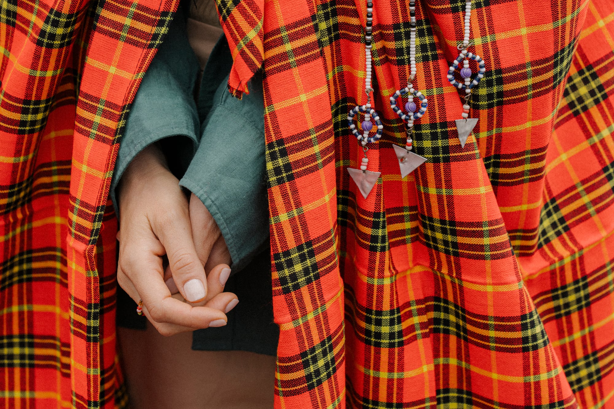 Close-up of hands under red Maasai shuka, traditional beaded jewelry visible.