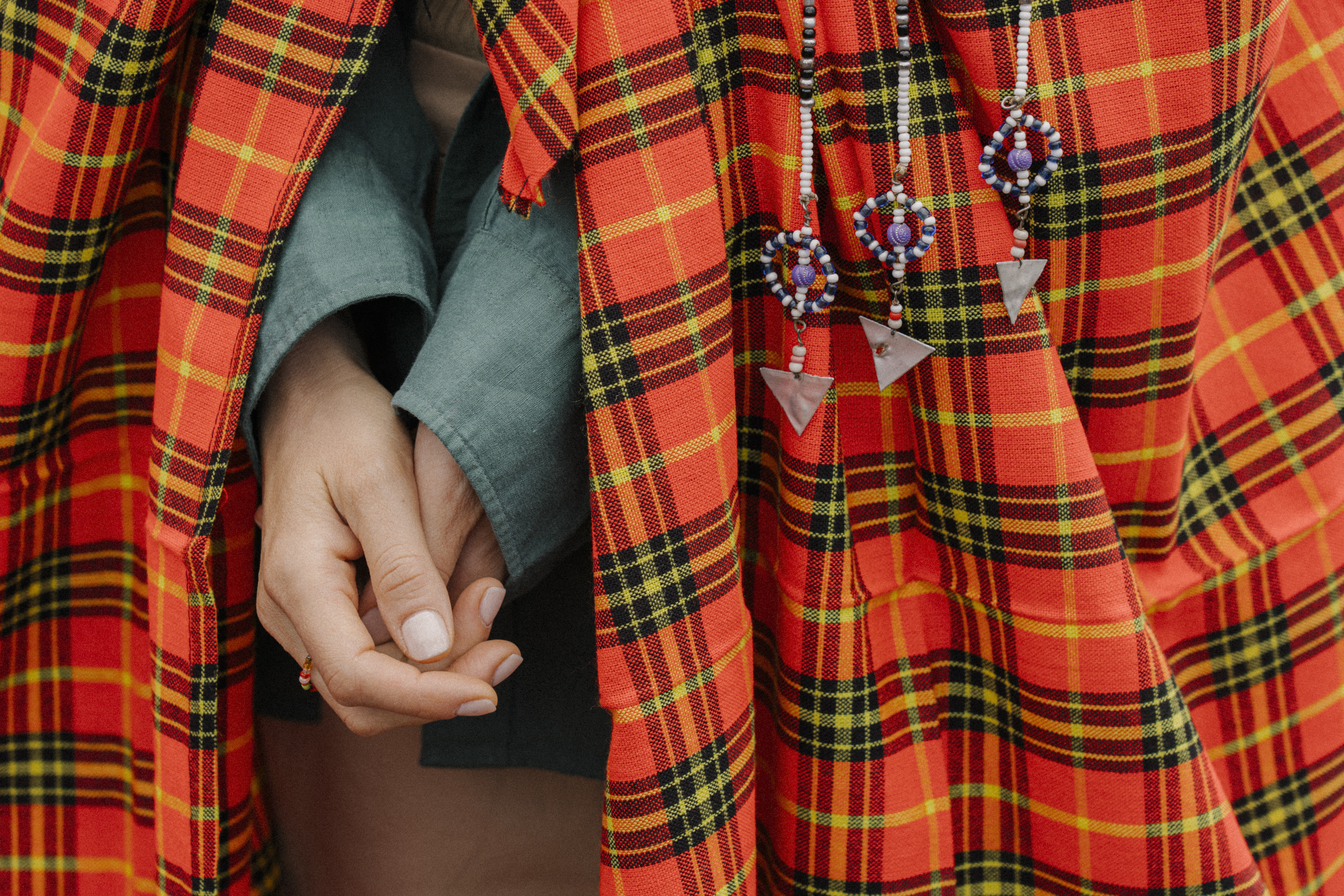 Close-up of hands under red Maasai shuka, traditional beaded jewelry visible.