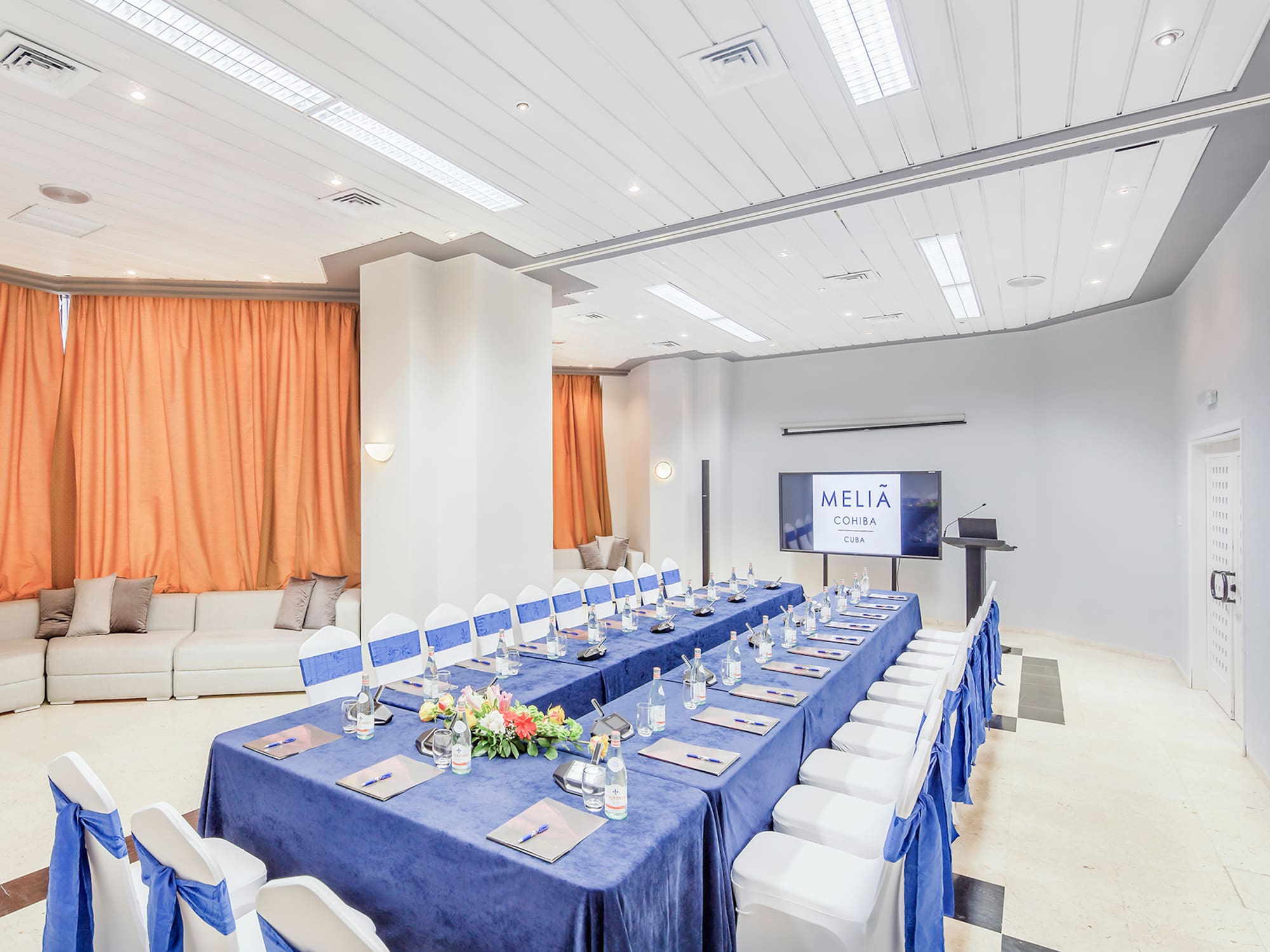 a long table with blue tablecloths and chairs in a room with a television