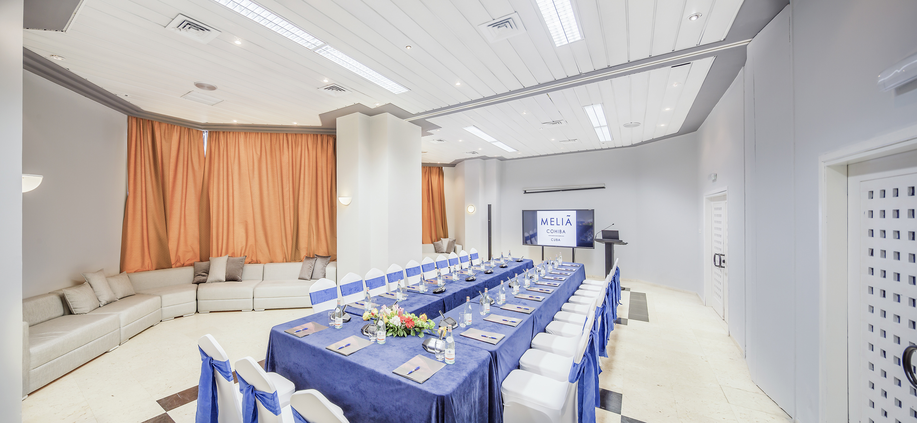 a long table with blue tablecloths and chairs in a room with a television