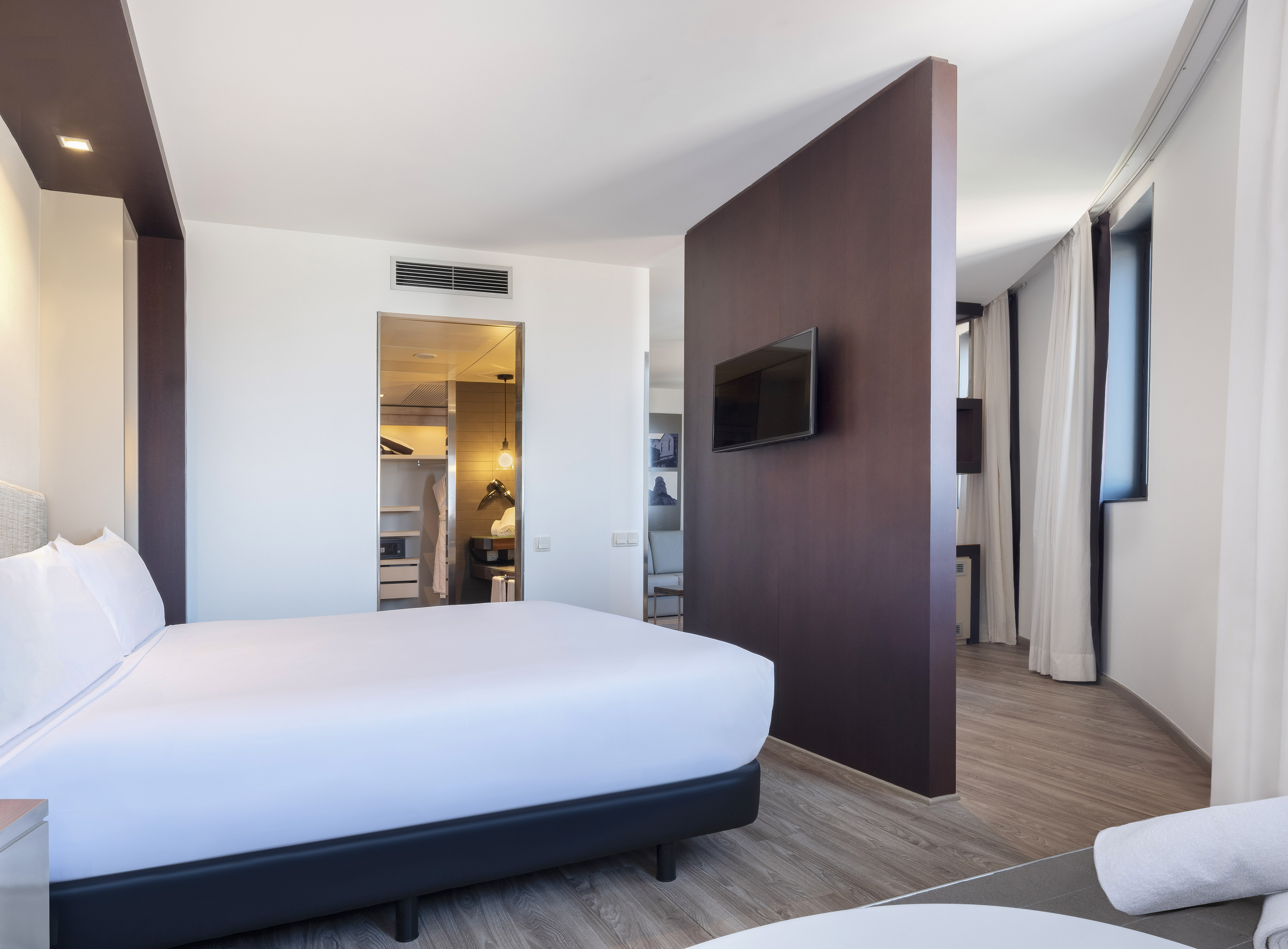Modern hotel bedroom with king bed, flat-screen TV, and walk-in closet.
