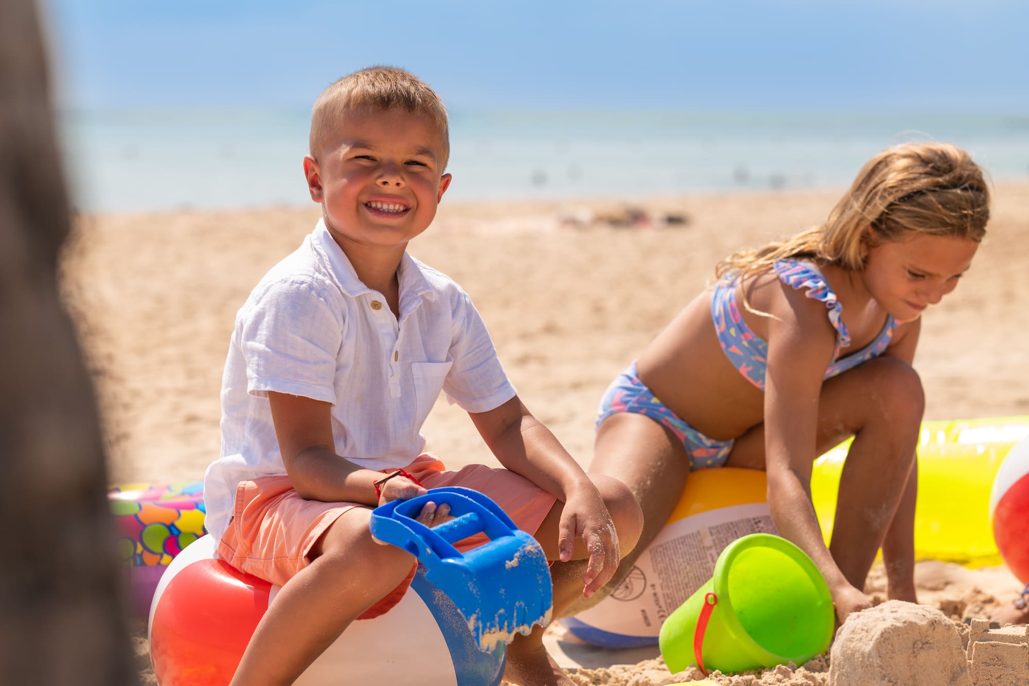 Niño sonriente y niña jugando con juguetes de arena en la playa.