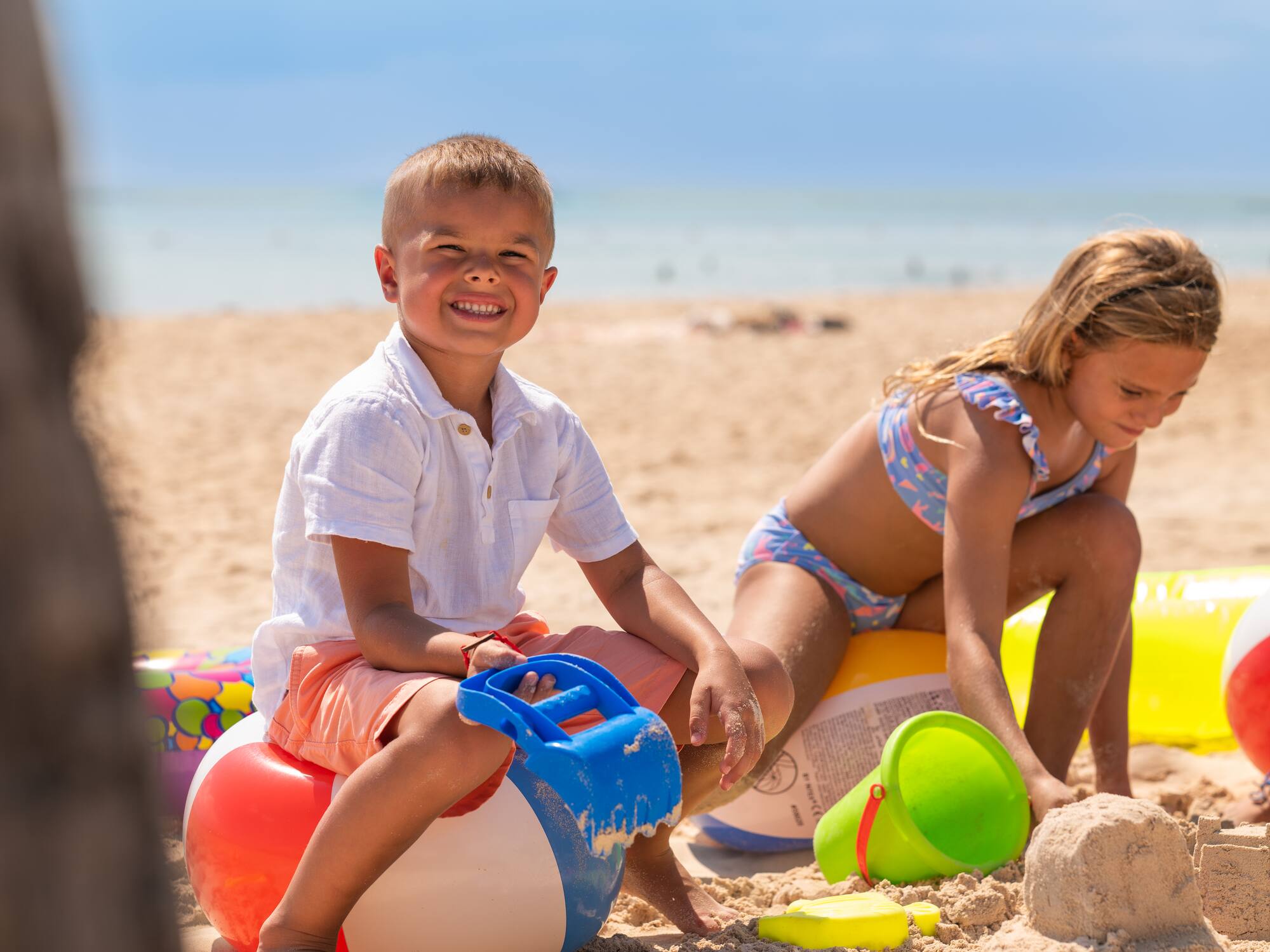 a boy and girl sitting on colorful balls on a beach