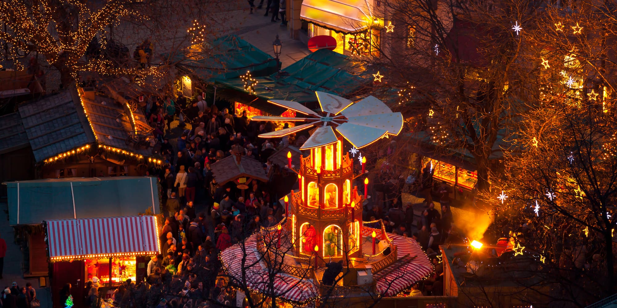 Mercado navideño nocturno con pirámide iluminada, puestos y gente.